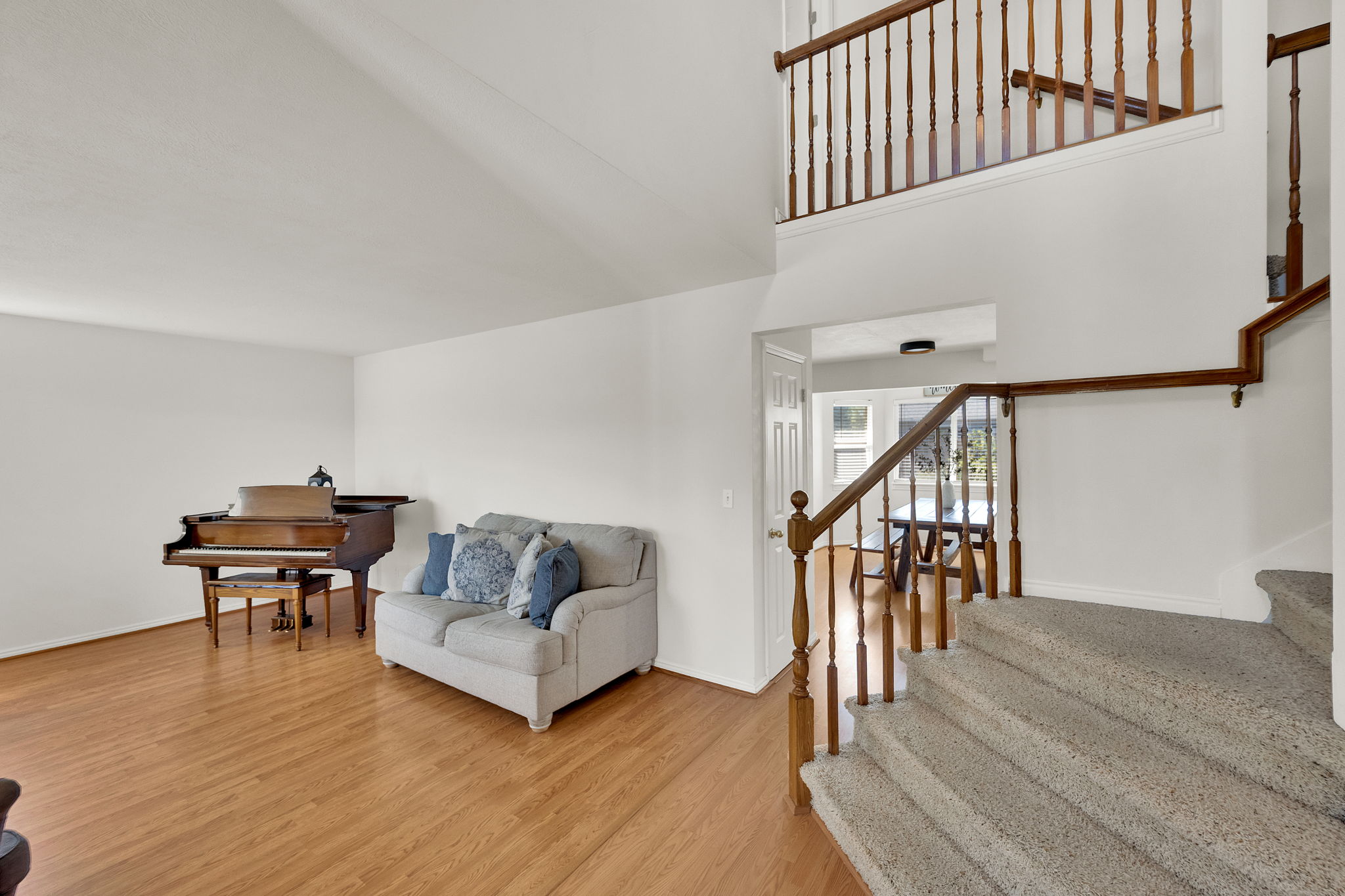 Interior space featuring vaulted ceilings, wood-finish flooring, a carpeted staircase with wood banister, and an open doorway leading to another room