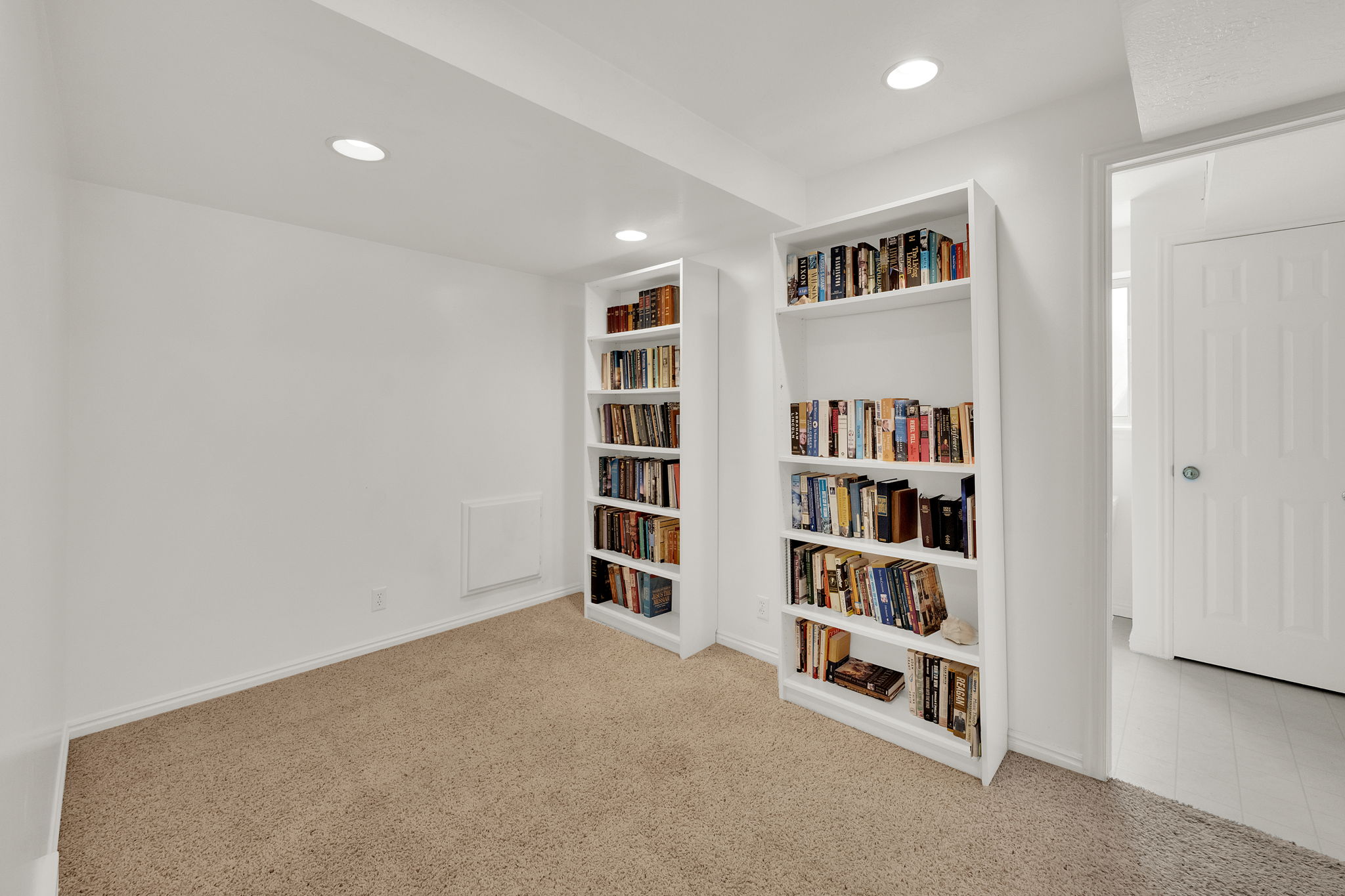 Built-in shelving units with recessed lighting and neutral carpeting