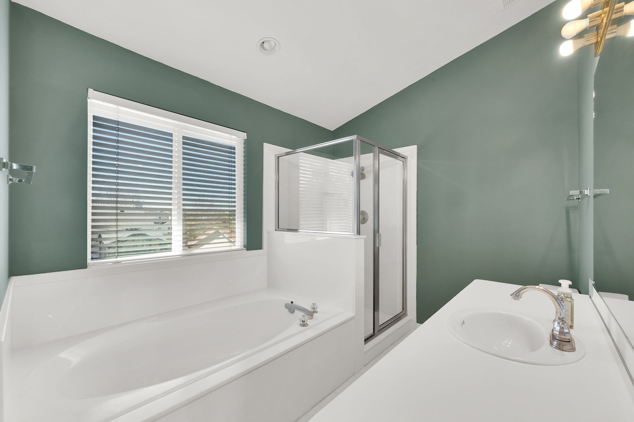 Bathroom featuring a built-in tub, separate glass-enclosed shower, a vanity with an integrated sink, and an overhead light fixture