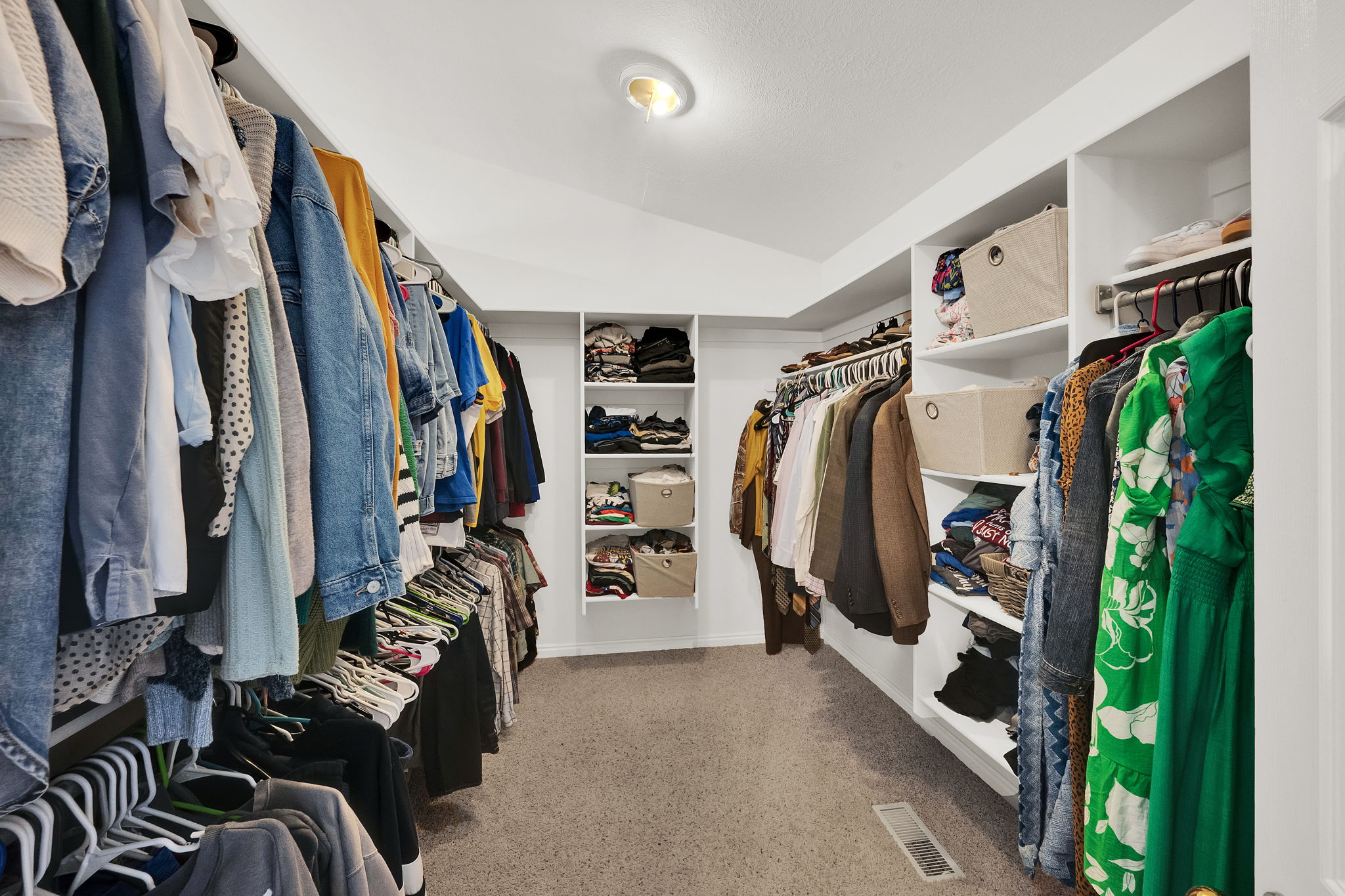 Spacious walk-in closet featuring extensive built-in shelving, multiple hanging rods, and recessed lighting