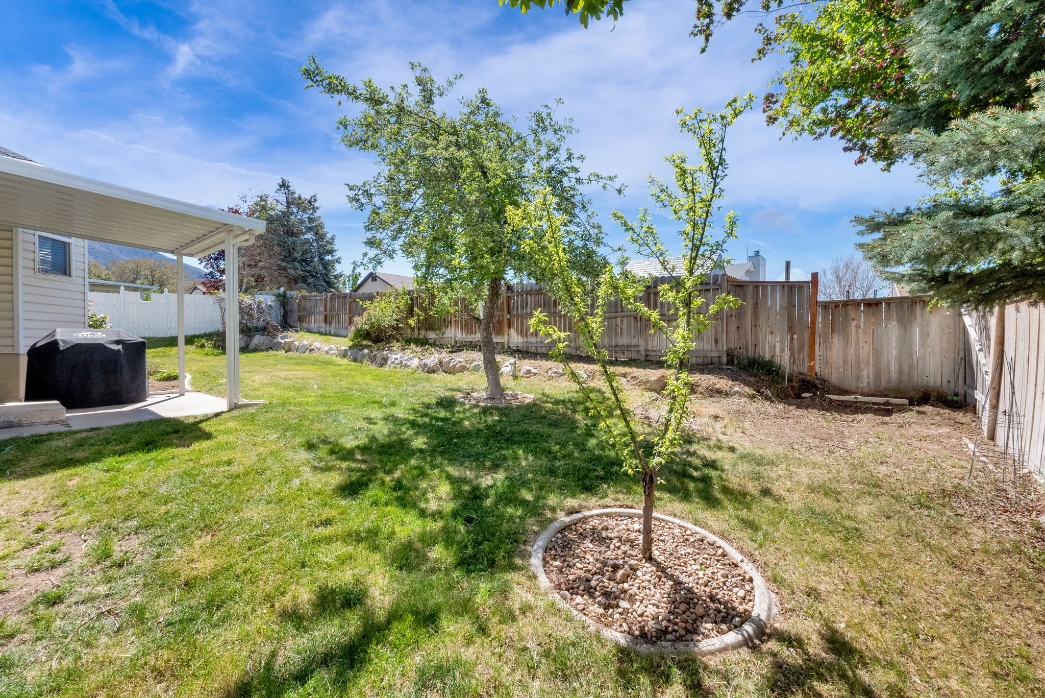 Spacious backyard featuring a covered patio, manicured lawn, and mature trees