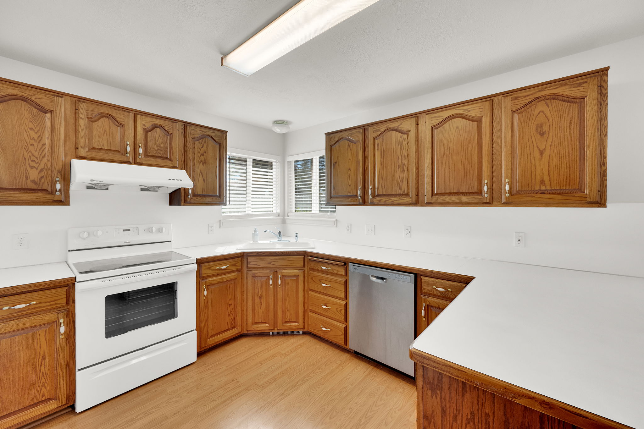 Kitchen featuring wood-finish cabinetry, white countertops, white electric range, and stainless steel dishwasher