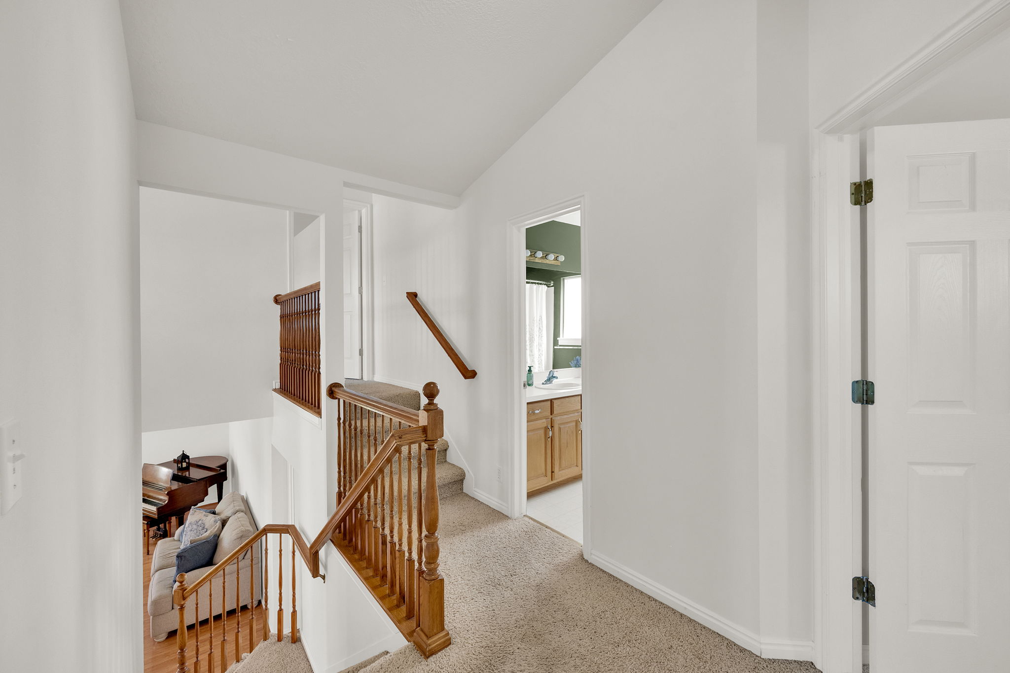 Upper landing with carpeted flooring and white painted walls, featuring a wood spindle railing and handrail