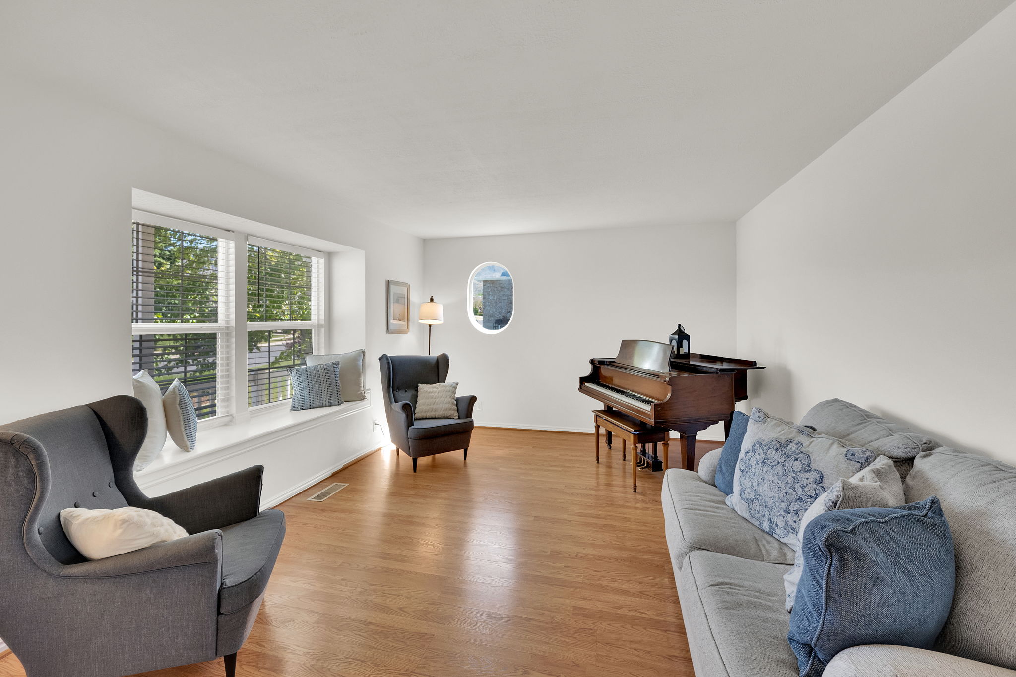 Expansive living area featuring wood-finish flooring, a broad bay window with a deep sill, and an oval accent window