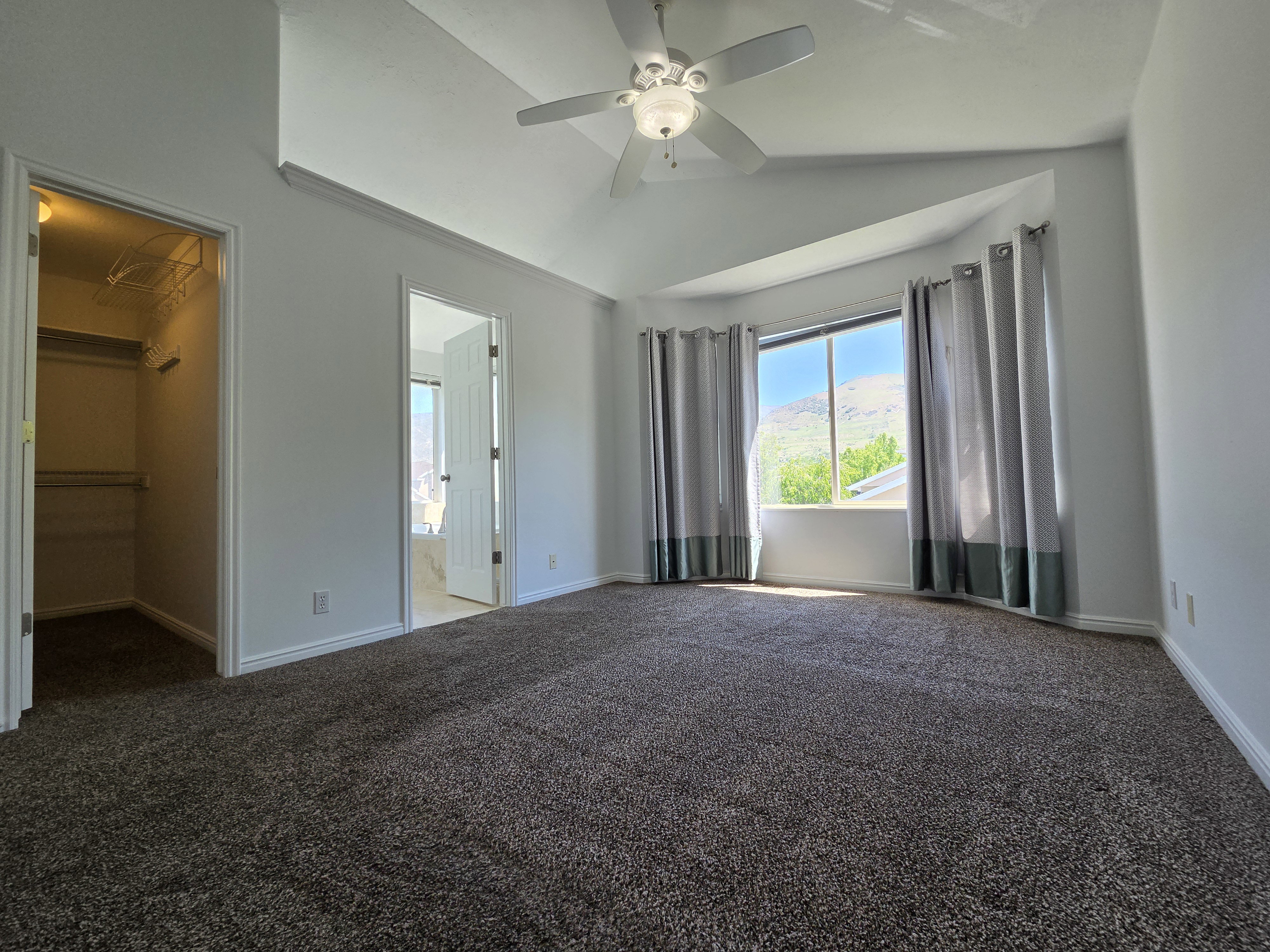 Spacious room featuring vaulted ceilings and a ceiling fan, bay windows, and neutral carpet flooring