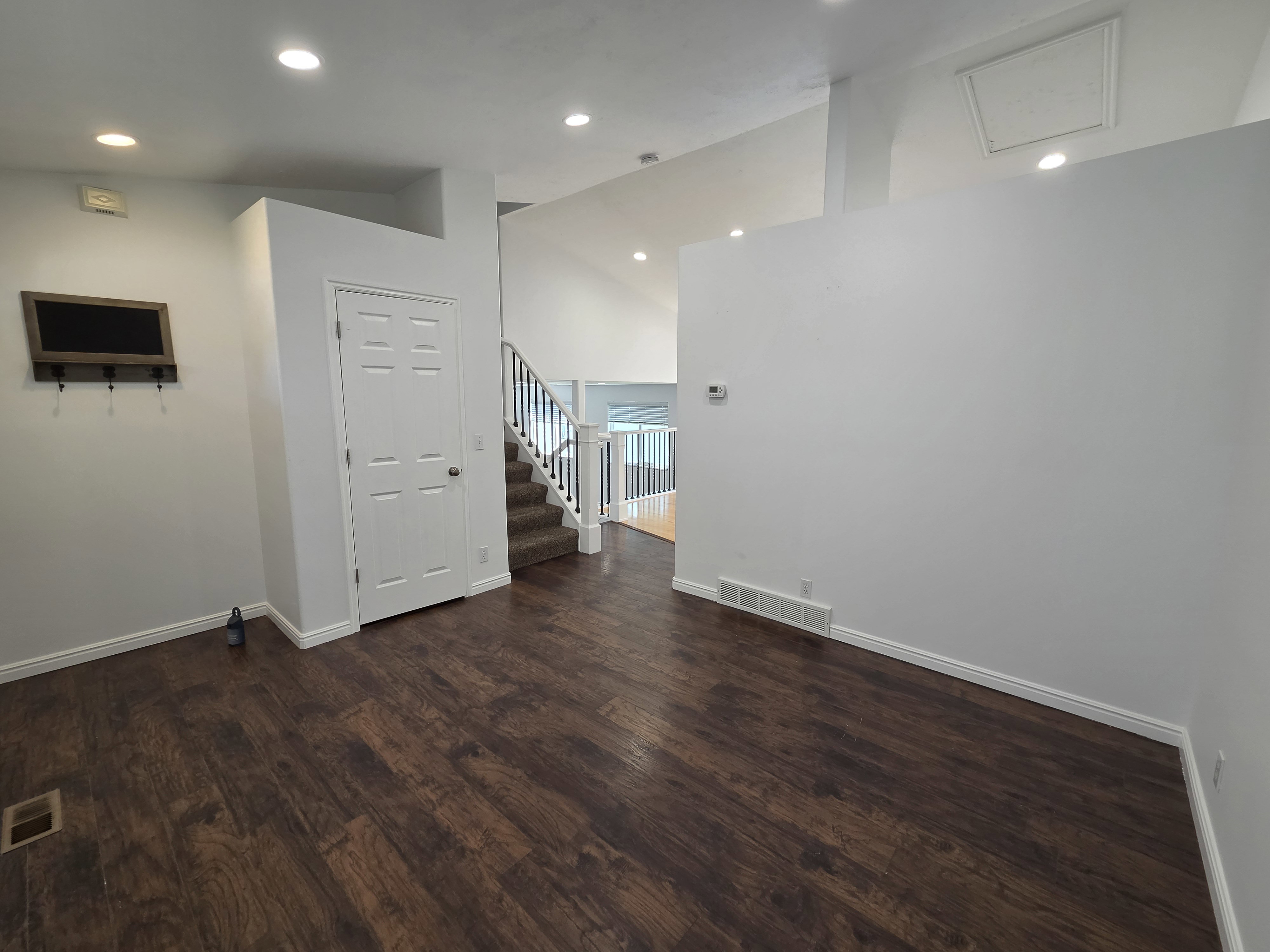 Spacious interior featuring wood-finish flooring, recessed lighting, white trim, and a prominent staircase with white railings