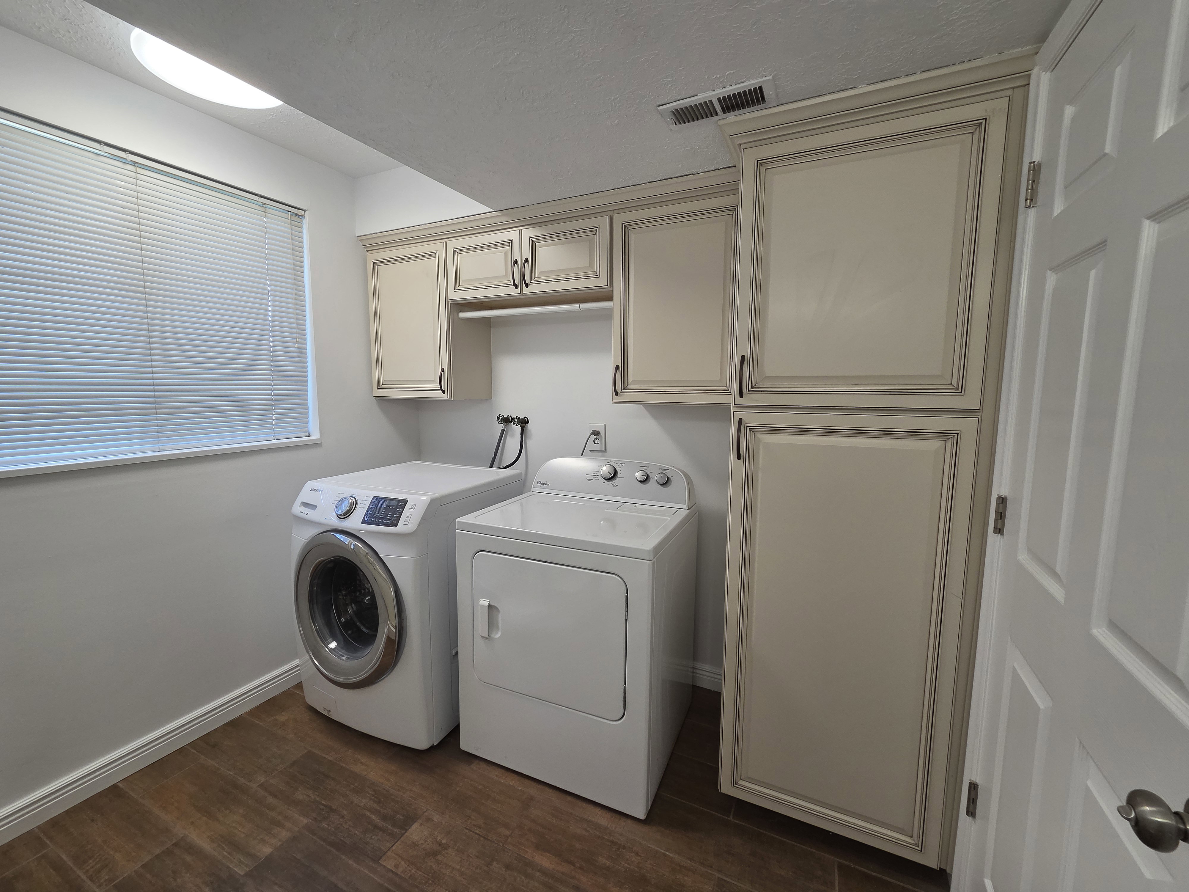 Dedicated utility space featuring extensive cabinetry, wood-finish flooring, a window with blinds, and ceiling illumination