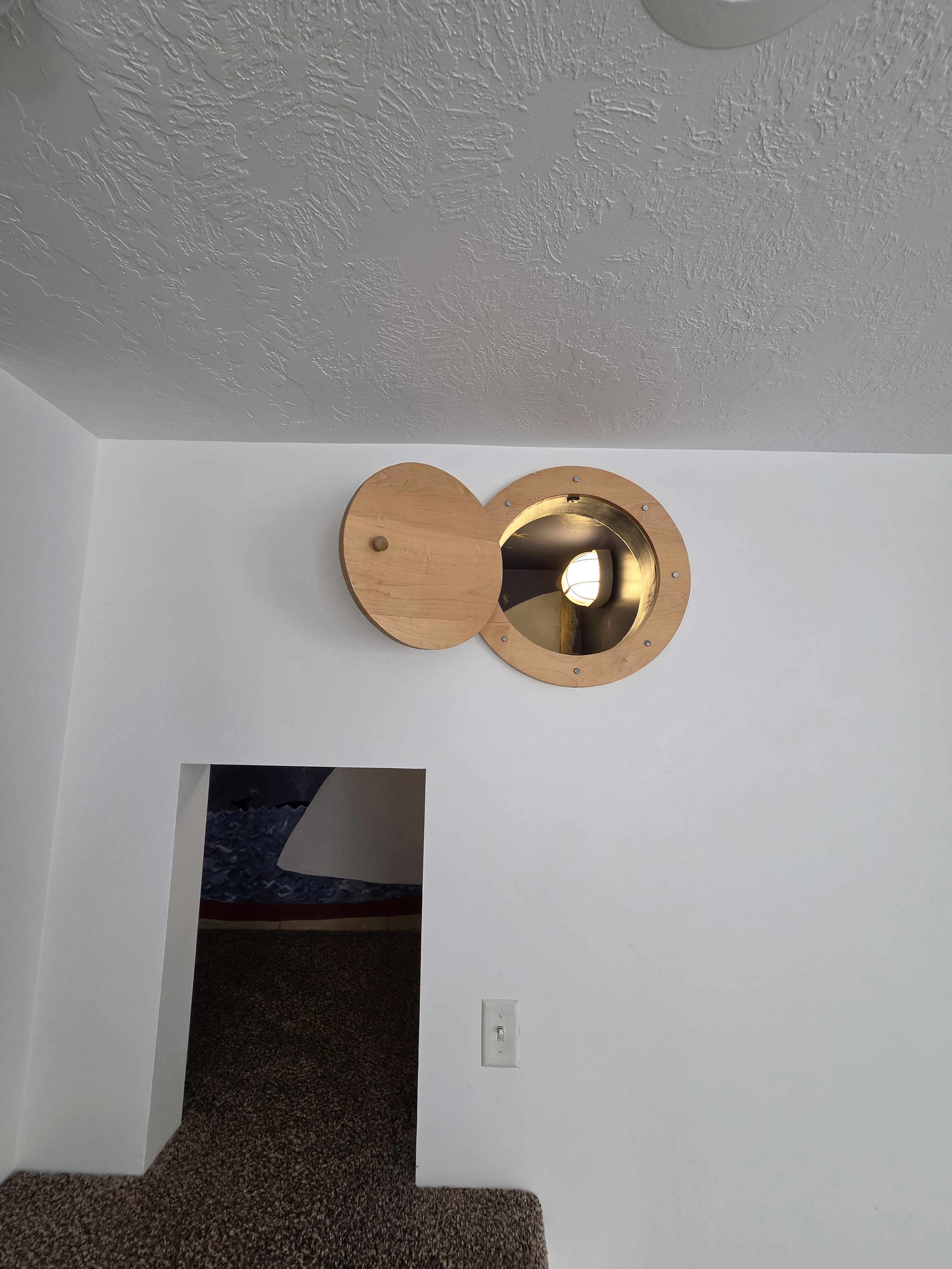 Circular wooden portal with a hinged cover and interior light fixture