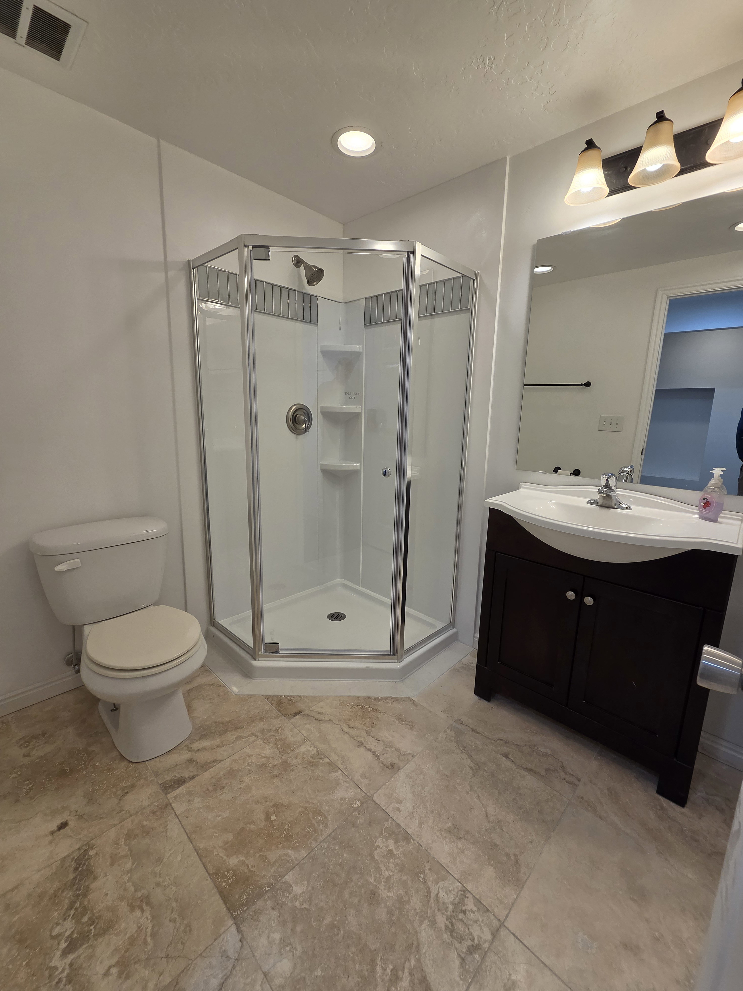 Full bathroom featuring a corner shower with glass enclosure, single vanity with a dark wood-finish cabinet, and a large wall mirror