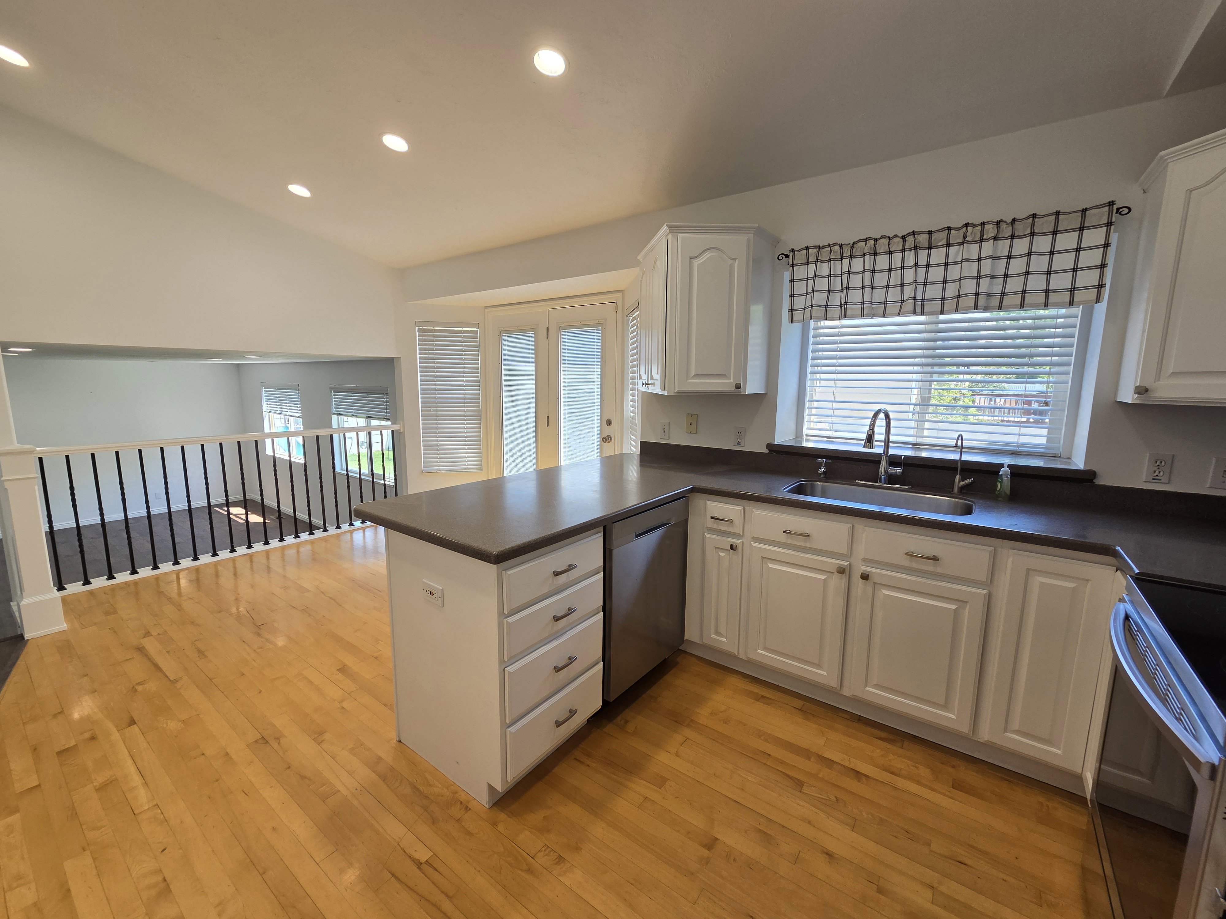 Kitchen featuring wood-finish flooring, white cabinetry, a central island with drawers, a stainless steel sink with a gooseneck faucet, and a window with horizontal blinds