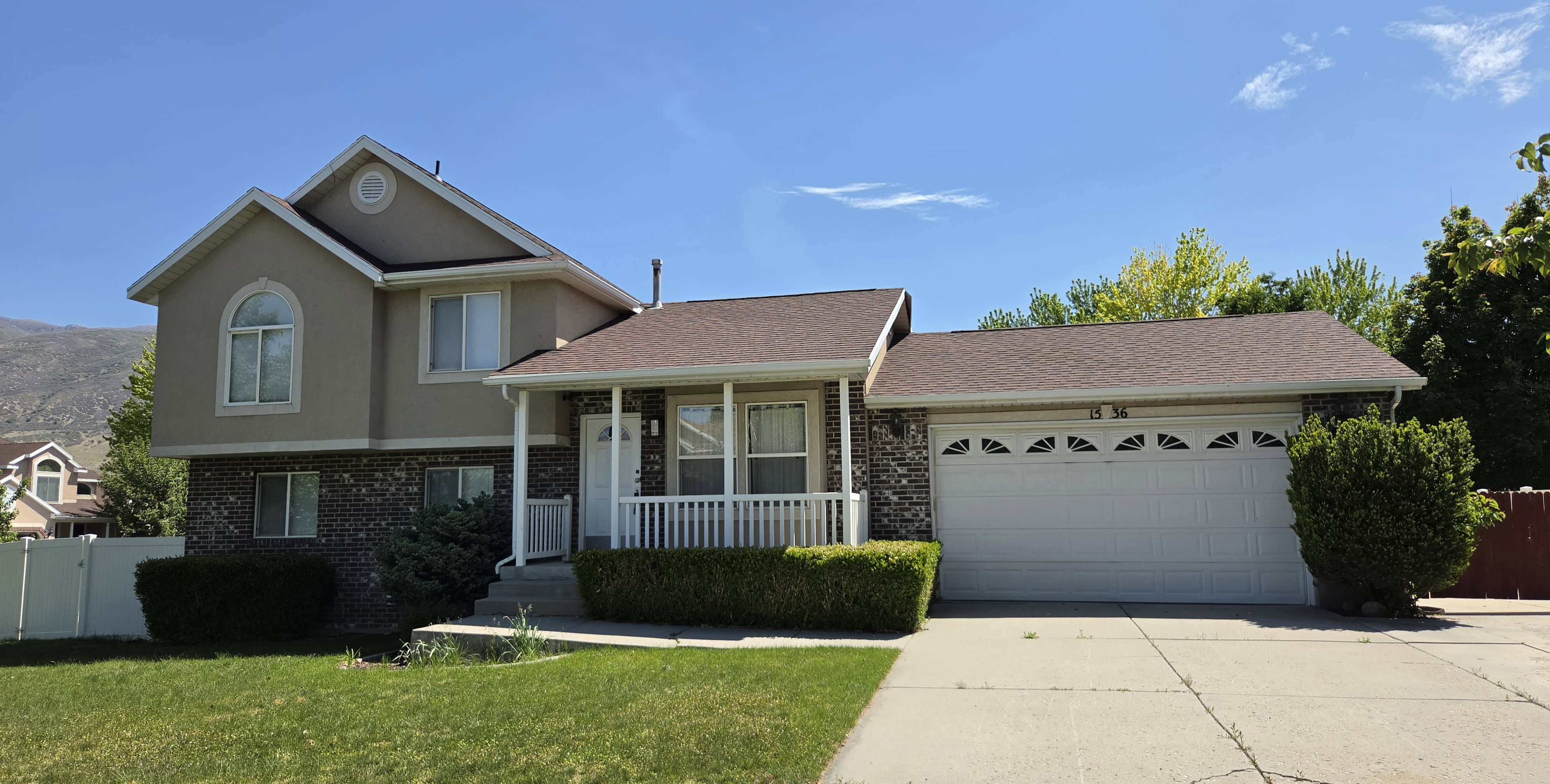 Two-story stucco and stone-veneer exterior featuring an arched window, covered front porch with white railing, and a two-car garage with decorative window inserts