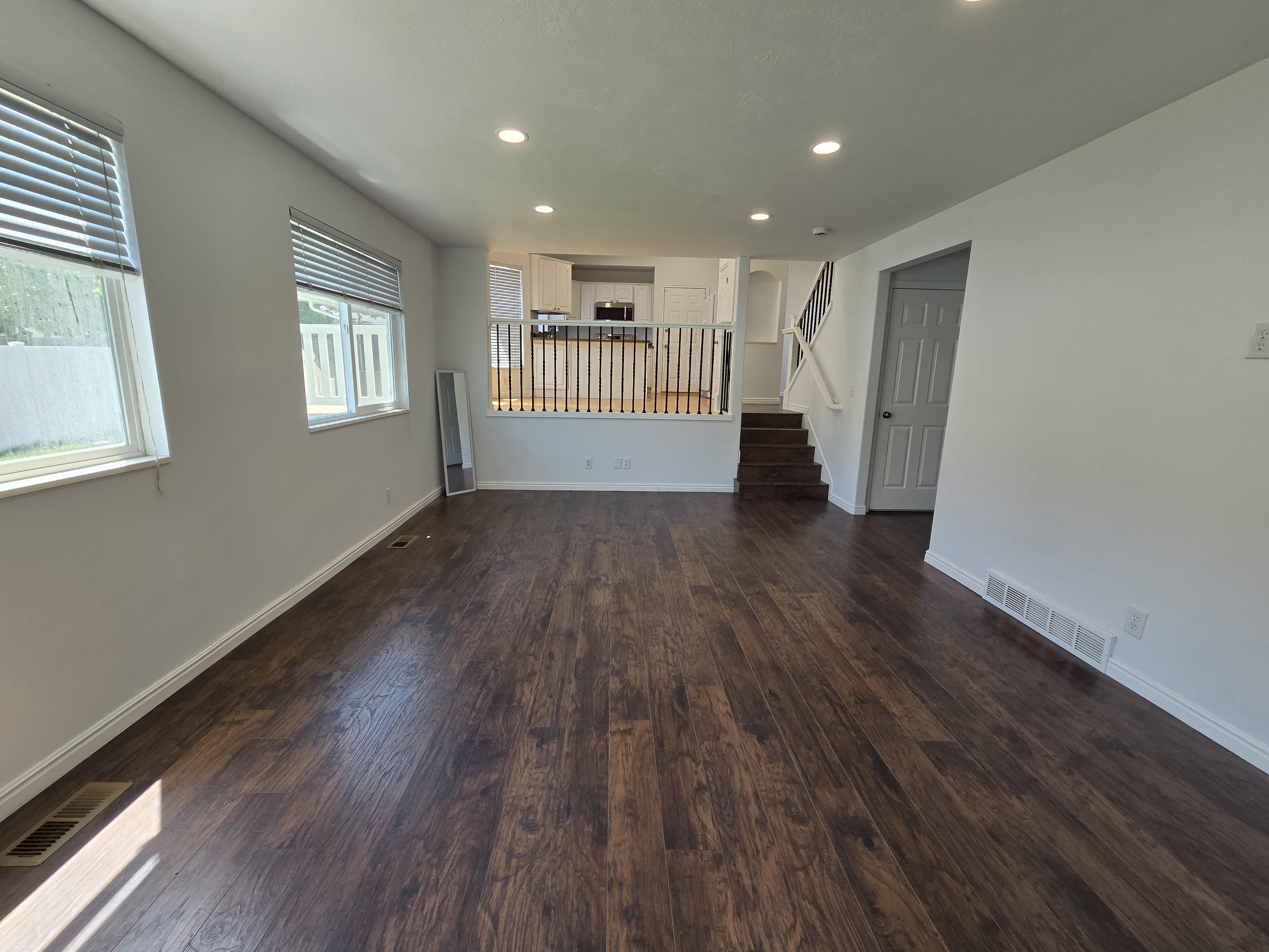 Spacious living area featuring rich wood-finish flooring, recessed lighting, and multiple windows with horizontal blinds