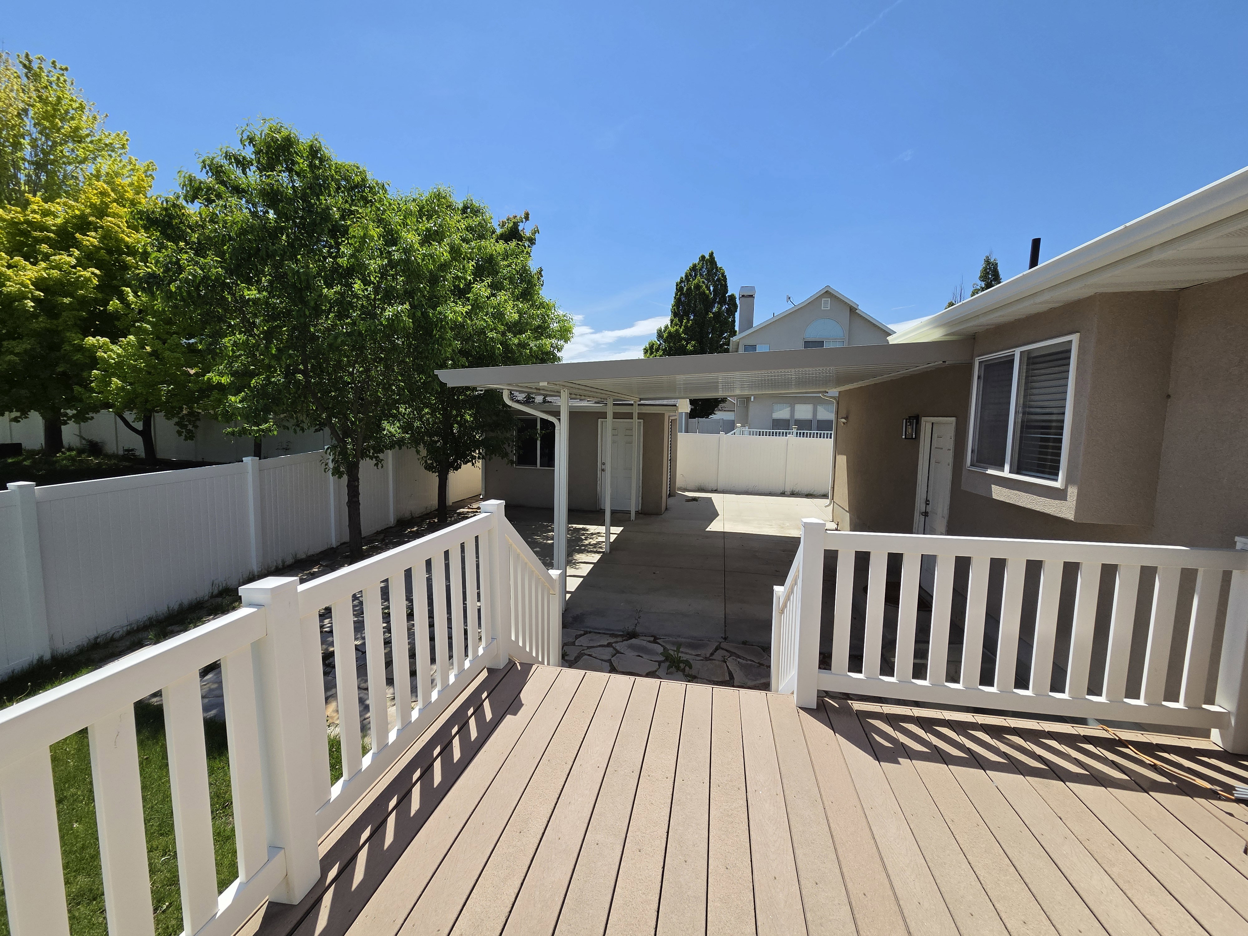 Expansive wood-finish deck with white railing, featuring a covered patio area and mature perimeter trees