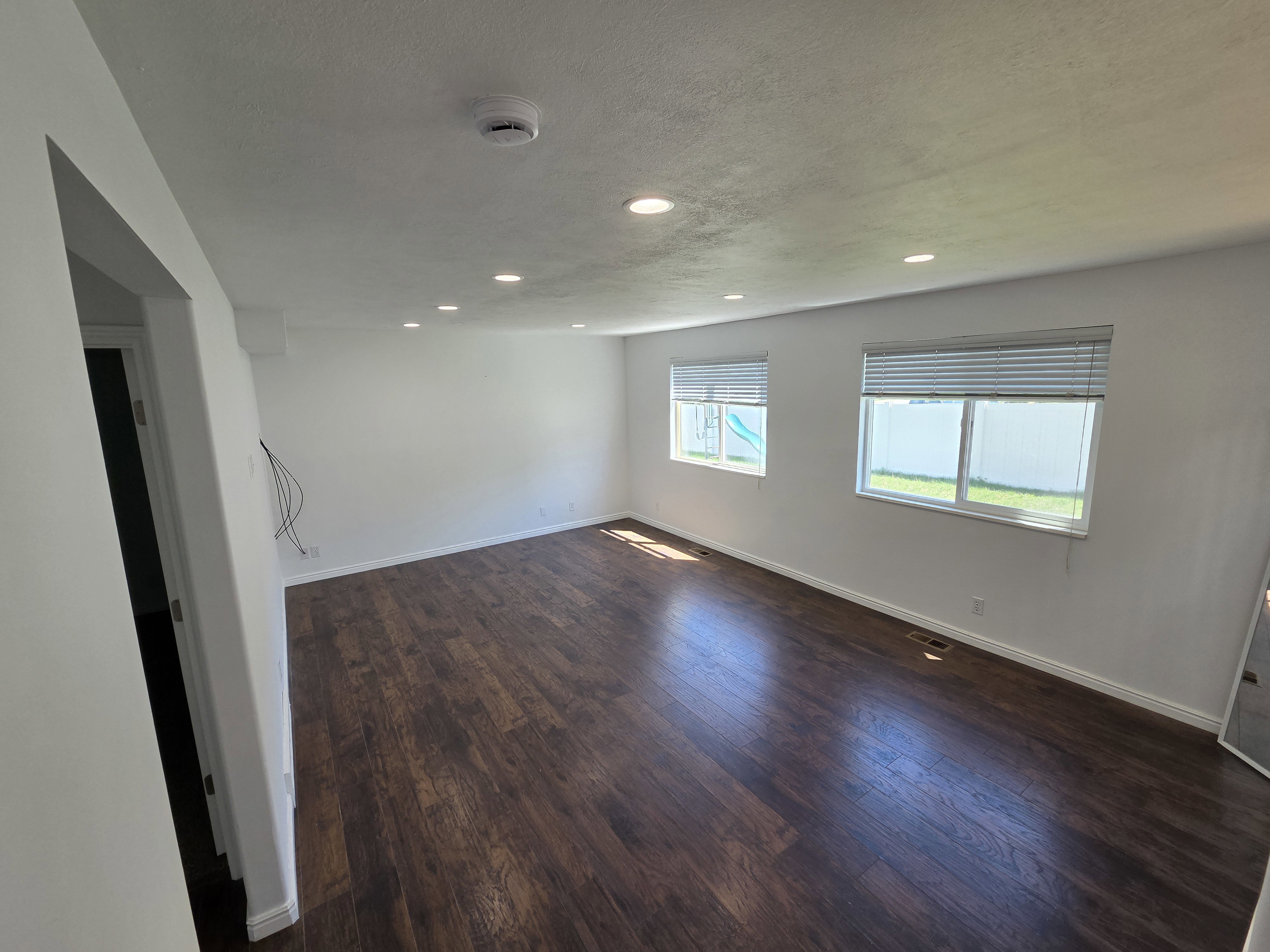 Spacious room featuring wood-finish flooring, recessed lighting, and two windows with blinds