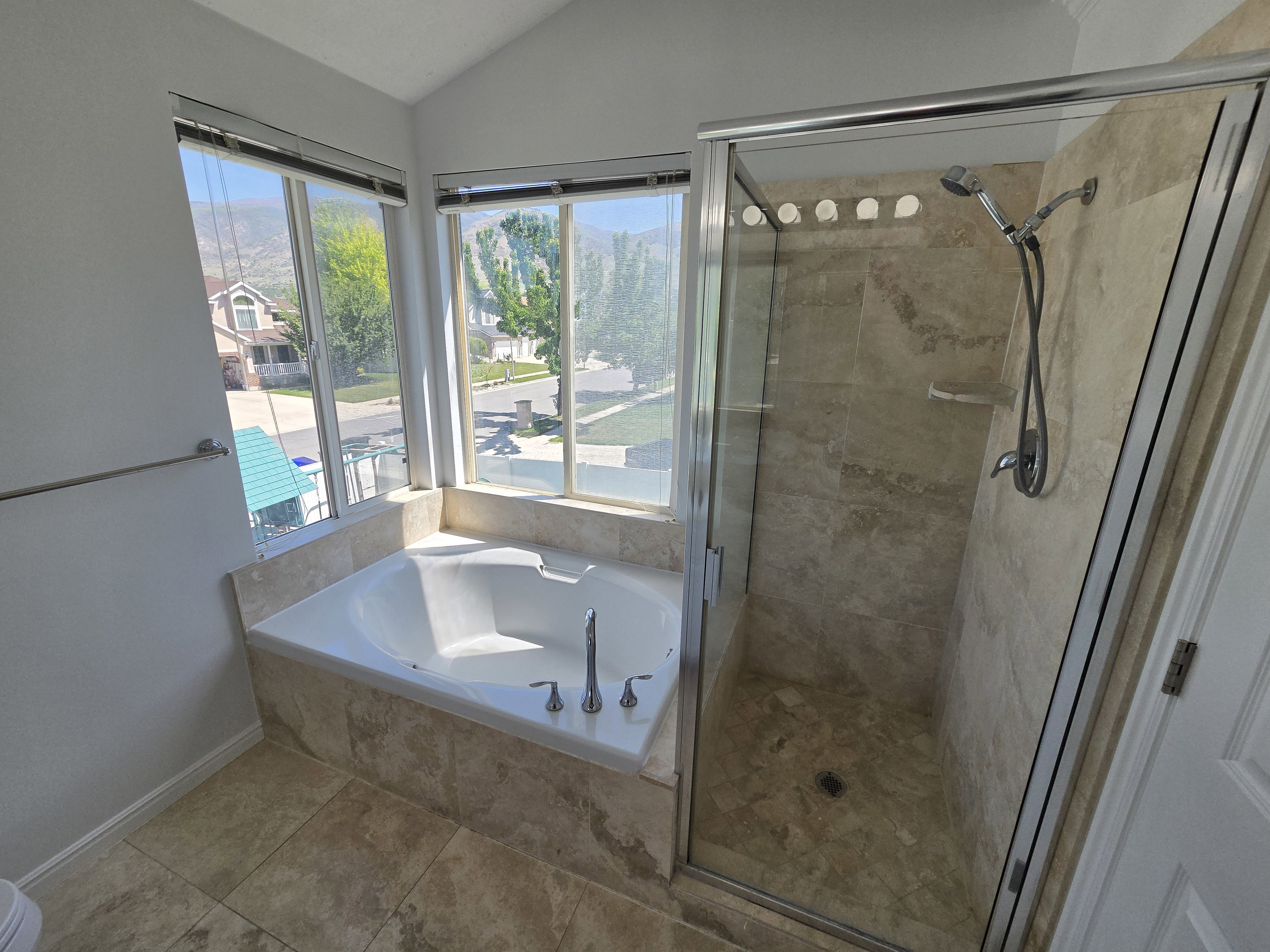 Spa-like bathroom with a built-in jetted tub, expansive windows, and a glass-enclosed shower featuring natural stone-finish tiling and a wall-mounted shower system