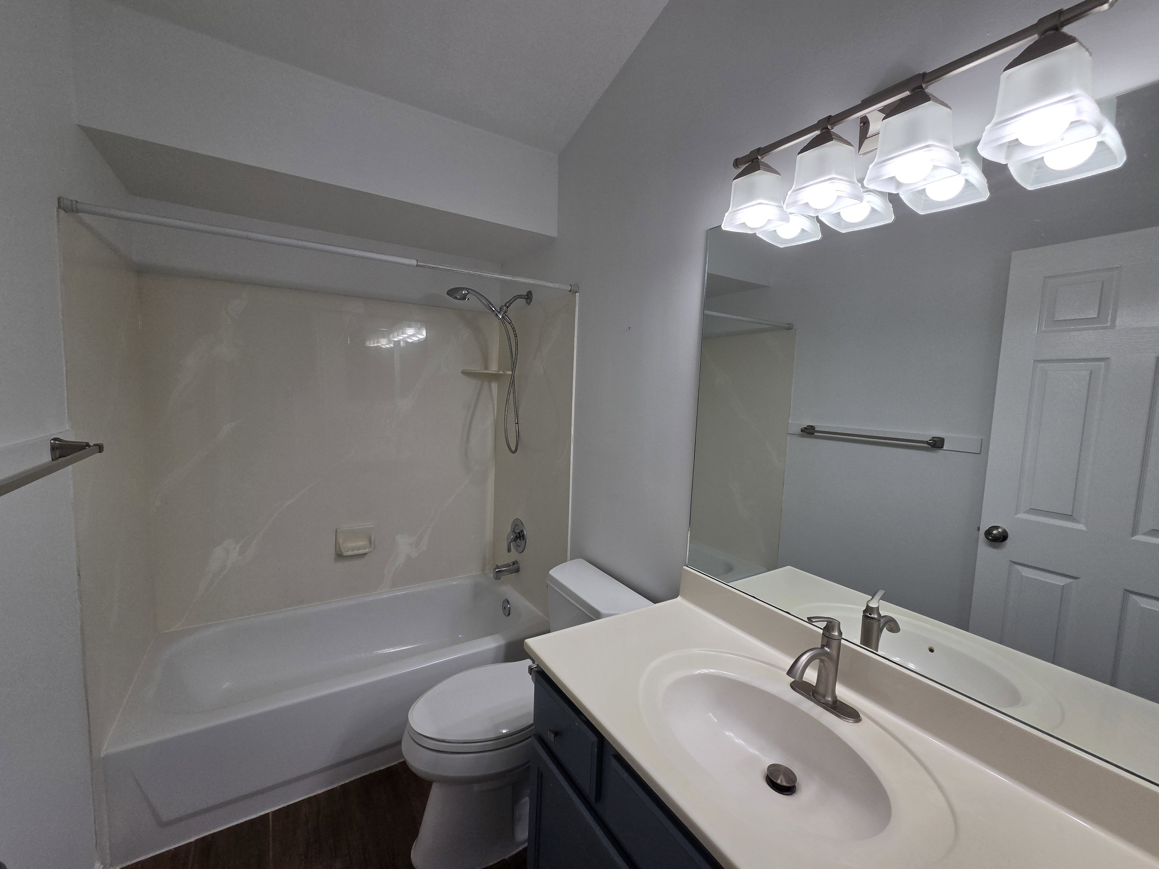 Bathroom featuring a combination shower and tub with a white surround, a single vanity with an integrated sink and light countertop, and wood-finish flooring