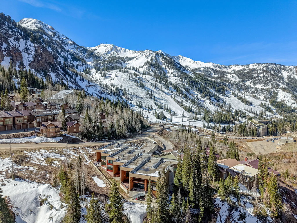 Expansive mountain landscape featuring snow-covered peaks, dense evergreen forests, and multiple residential structures