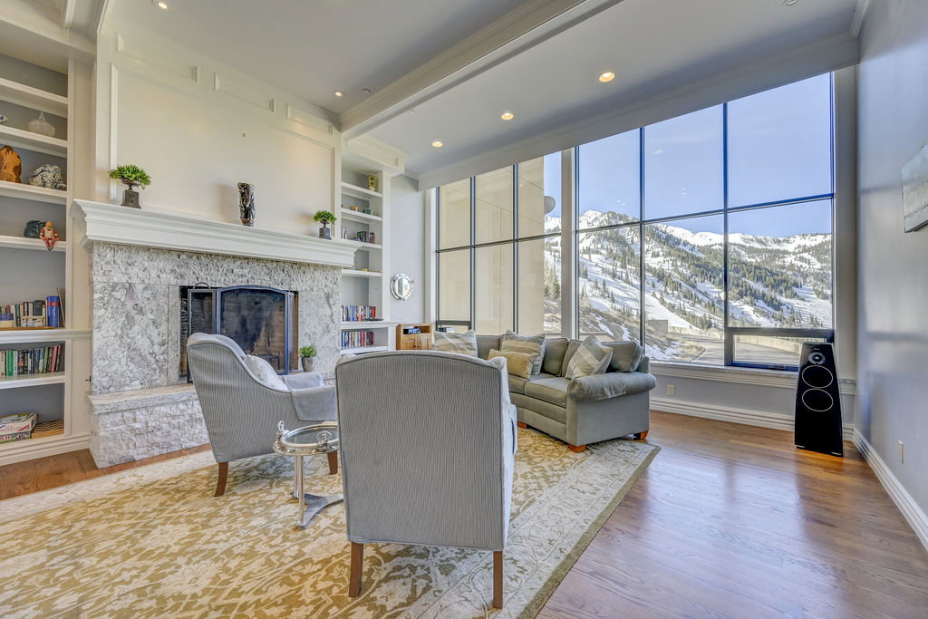 Living area featuring expansive floor-to-ceiling windows, a stone-clad fireplace, integrated built-in shelving, recessed lighting, and wood-finish flooring