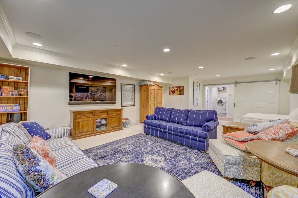 Spacious open-concept room featuring recessed lighting, a built-in wood bookshelf, wood-finish media console, and a ceiling-mounted sound system