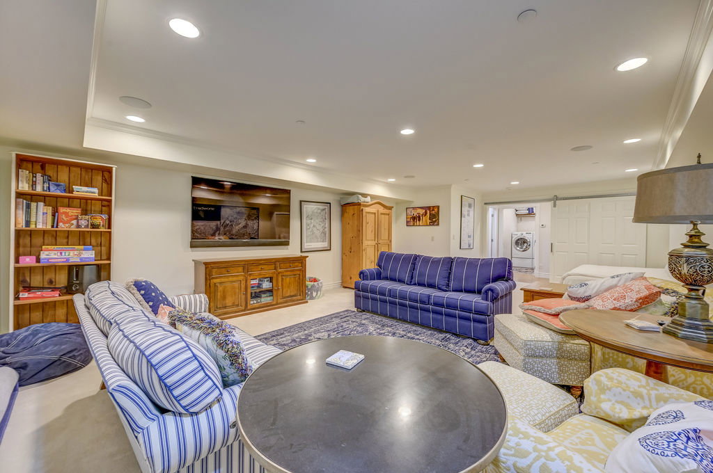Spacious entertainment room featuring recessed lighting, crown molding, a built-in wood bookshelf, and barn door access to a laundry area with a visible washer and dryer
