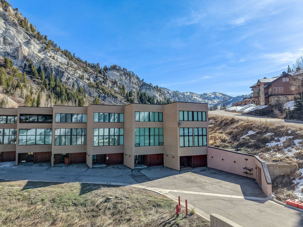 Contemporary multi-story building featuring extensive window placements, individual garage access, and a mountain backdrop