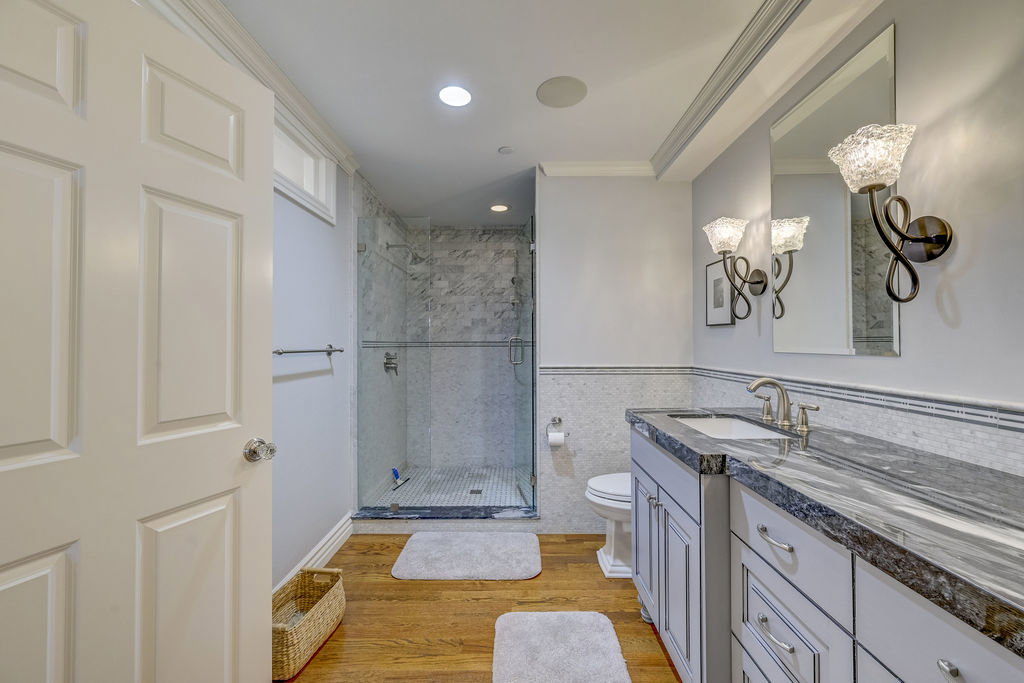 Bathroom featuring a glass-enclosed shower with tiled walls and floor, a vanity with a dark stone countertop, an undermount sink, and wood-finish flooring