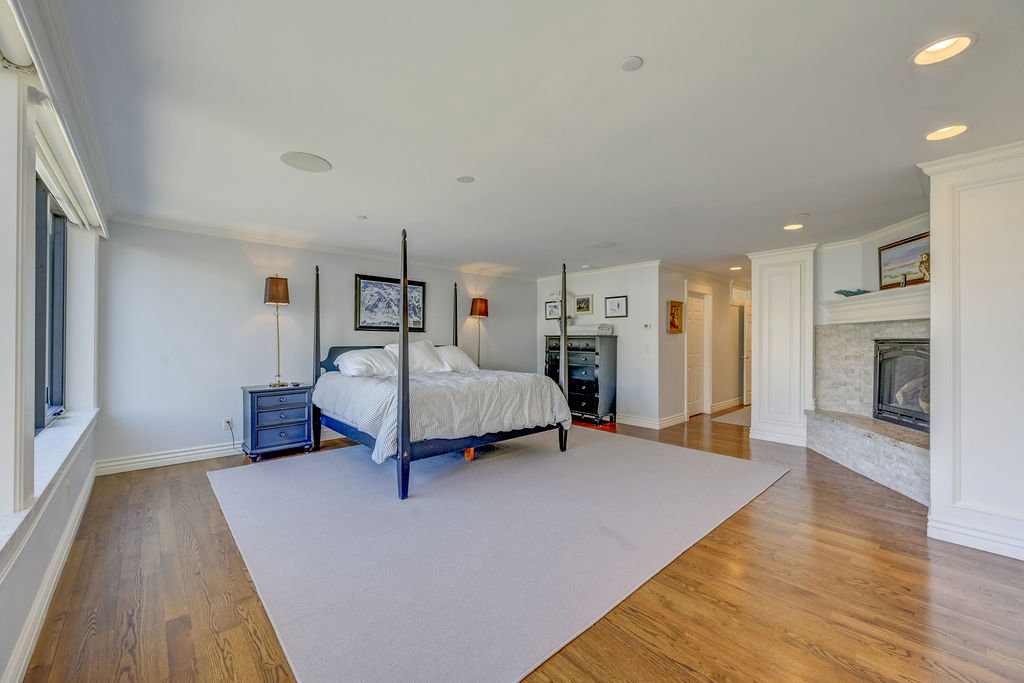 Spacious interior featuring hardwood flooring, a gas fireplace with a stone hearth and surround, recessed lighting, crown molding, and large windows