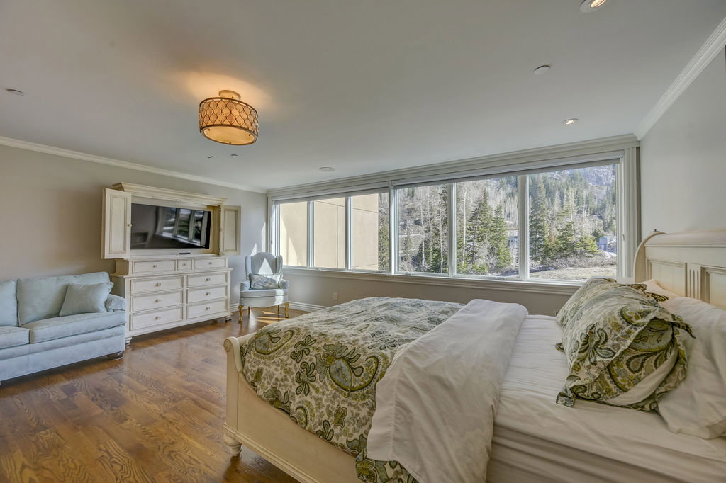 Hardwood flooring enhances this bedroom featuring a large picture window overlooking a wooded landscape