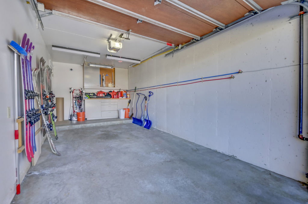 Concrete floor garage featuring a built-in workbench with storage cabinetry, overhead fluorescent lighting, and visible utility lines