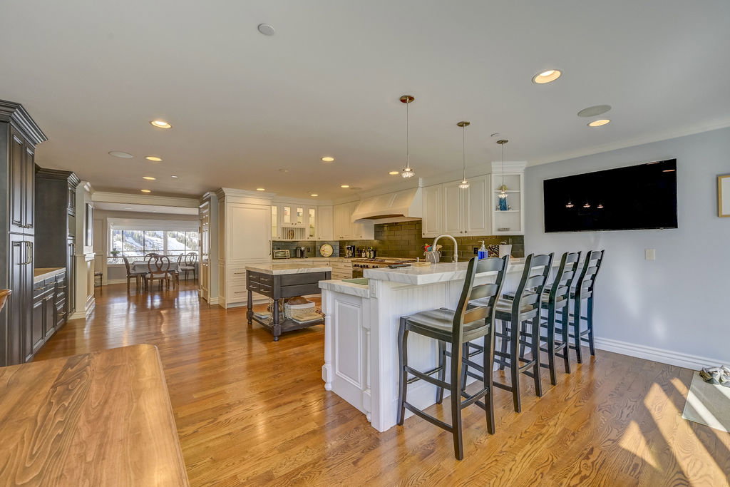 Open-concept kitchen featuring wood-finish flooring, recessed lighting, a large island with seating, white cabinetry, and a separate dining area with a prominent window