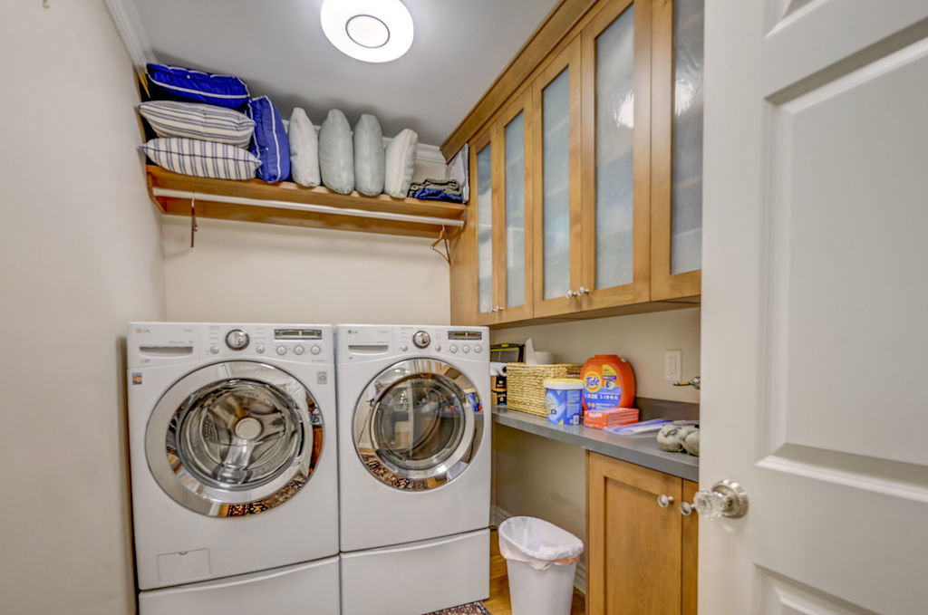Dedicated utility room featuring built-in cabinetry with frosted glass inserts, a built-in countertop, and an overhead storage shelf