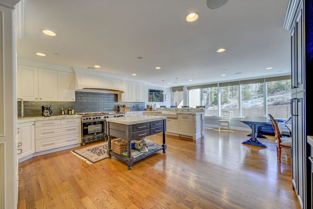 Expansive kitchen featuring wood-finish flooring, white cabinetry, a large range with a custom hood, and a dark-toned island with a stone countertop