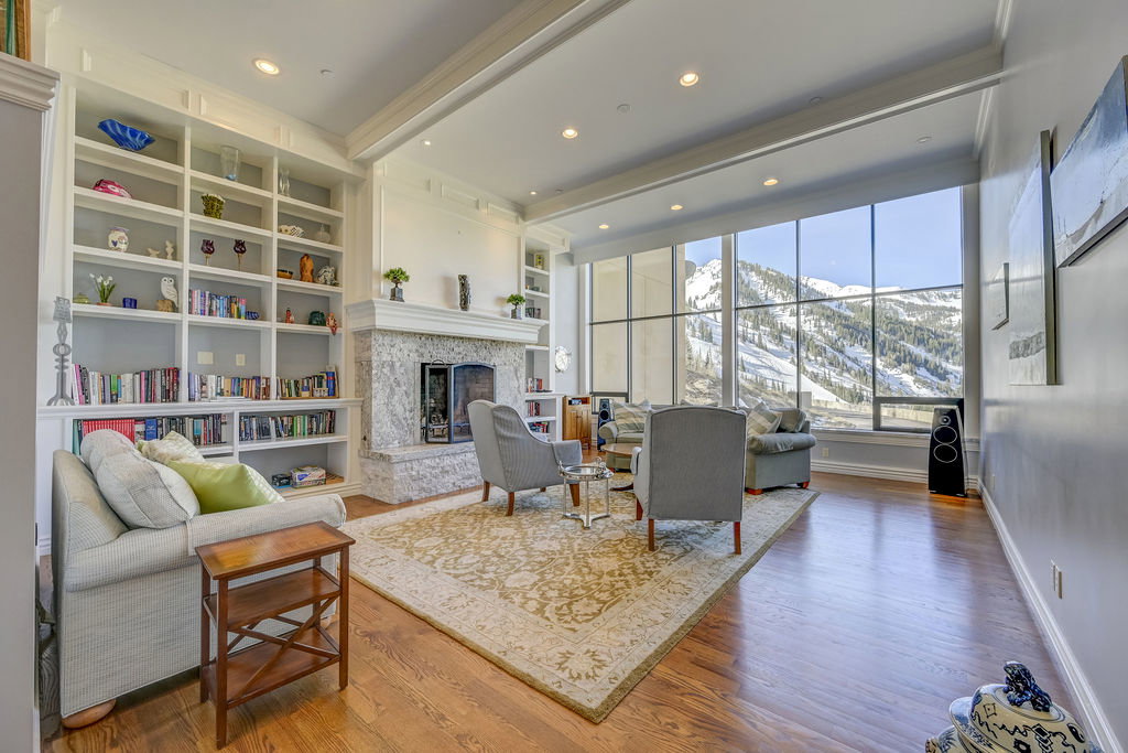 Spacious living area featuring expansive windows, a stone fireplace, built-in shelving, hardwood flooring, and recessed lighting