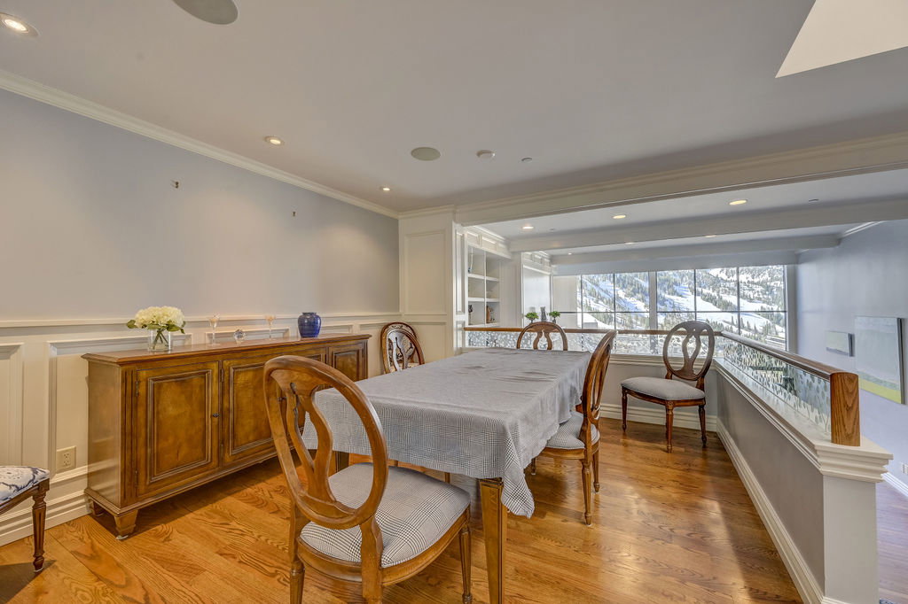 Formal dining area featuring hardwood flooring, wainscoting, recessed lighting, and a glass-paneled railing overlooking an expansive window with a mountain backdrop