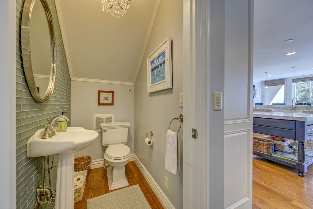 Pedestal sink with polished nickel faucet, glass subway tile accent wall, hardwood flooring, and a crystal chandelier