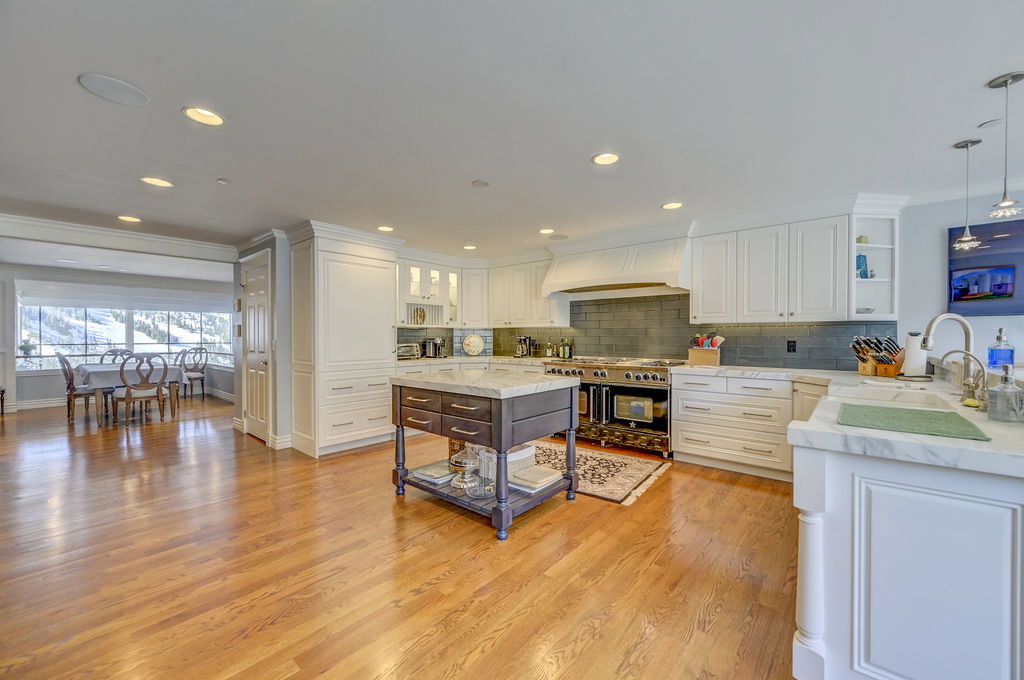 Gourmet kitchen featuring white cabinetry, light wood-finish flooring, a central island with a stone countertop, a large range with a custom hood, and a dining area with expansive windows