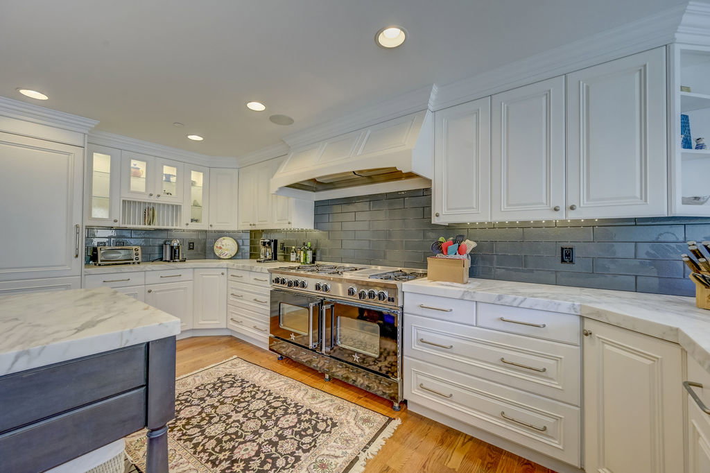 Gourmet kitchen featuring a professional-grade stainless steel range with double ovens, a custom range hood, and a dark tile backsplash