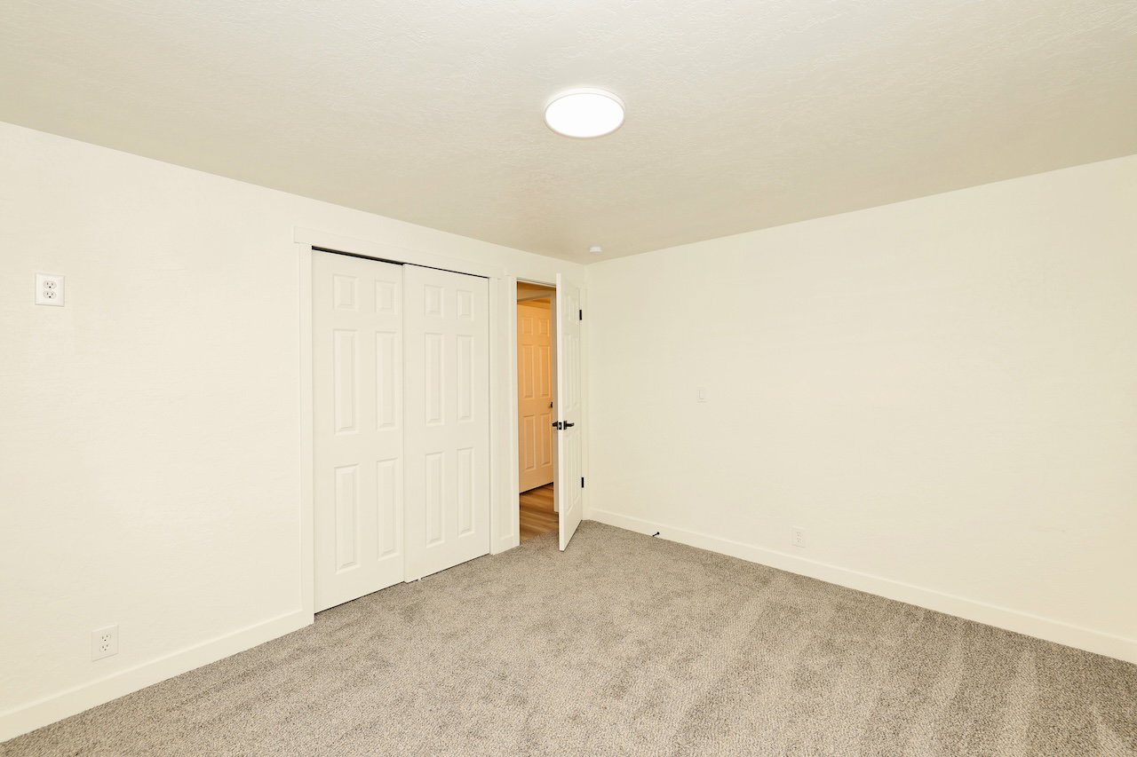 Spacious room featuring neutral carpeting, light cream walls, white trim, a flush-mount ceiling light, and a bi-fold closet door