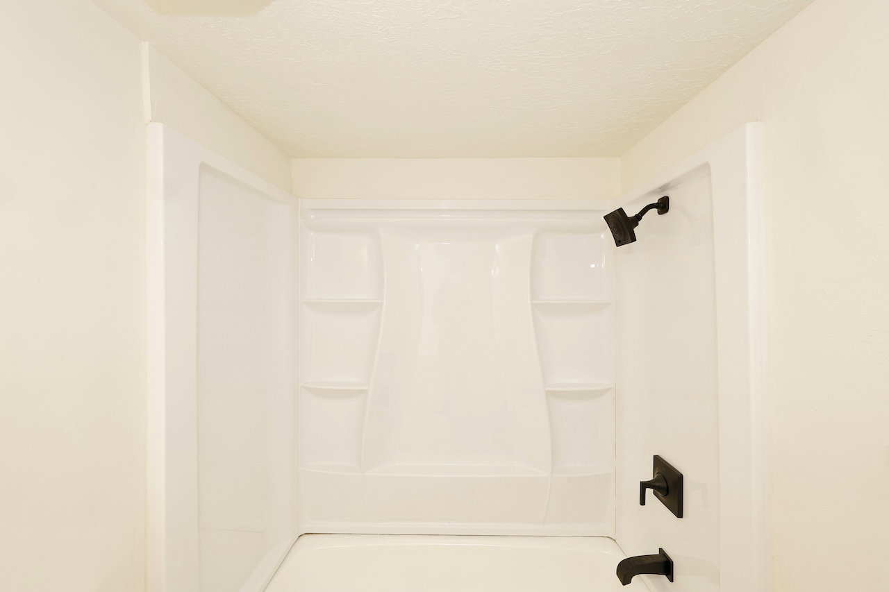 Bathtub-shower combination featuring a white surround with built-in shelving, matte black showerhead, and coordinating matte black faucet