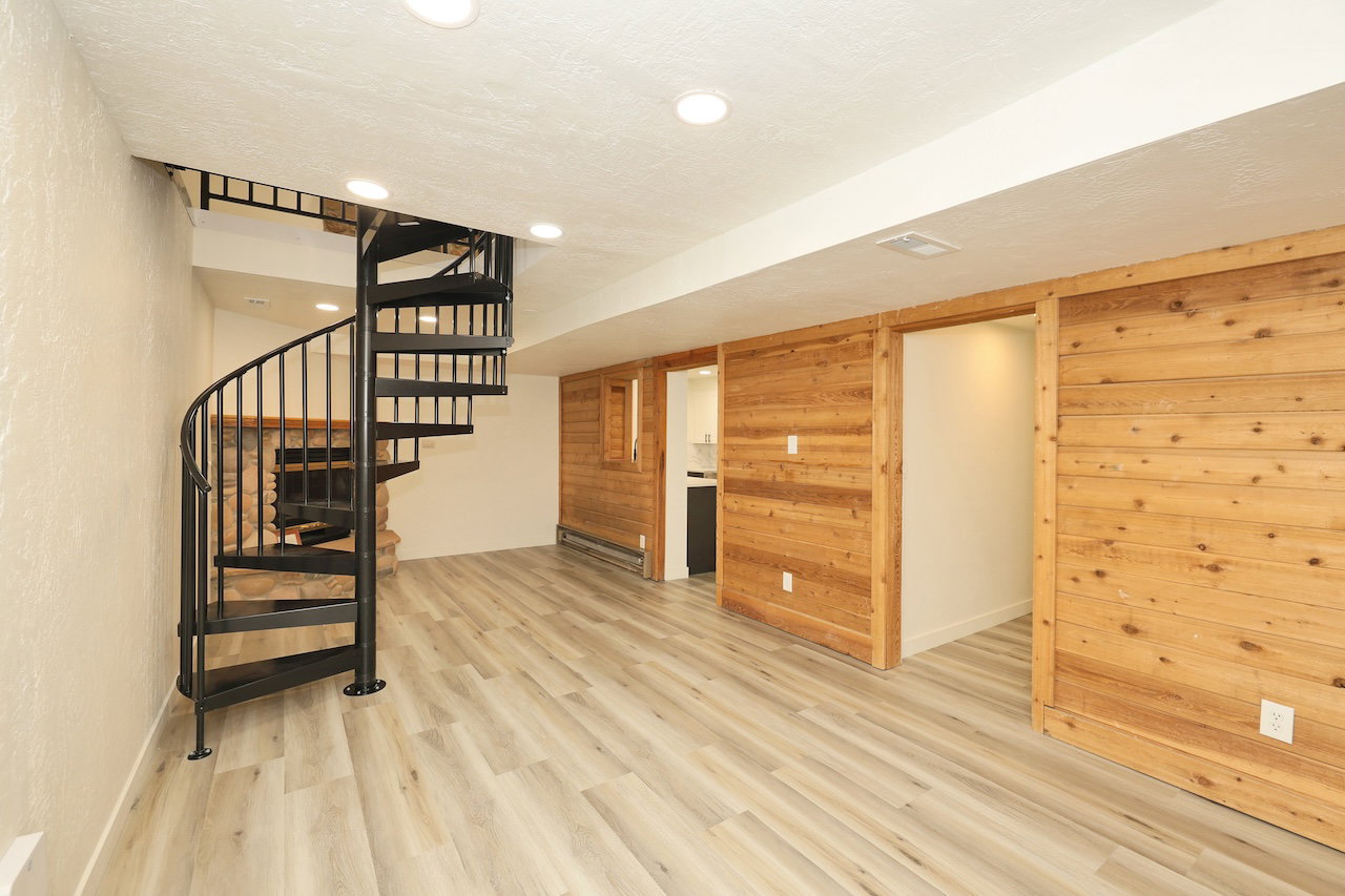 Open-concept room featuring a black metal spiral staircase, light wood-finish flooring, recessed lighting, and natural wood paneling with two sliding barn doors