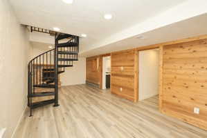 Open-concept room featuring a black metal spiral staircase, light wood-finish flooring, recessed lighting, and natural wood paneling with two sliding barn doors