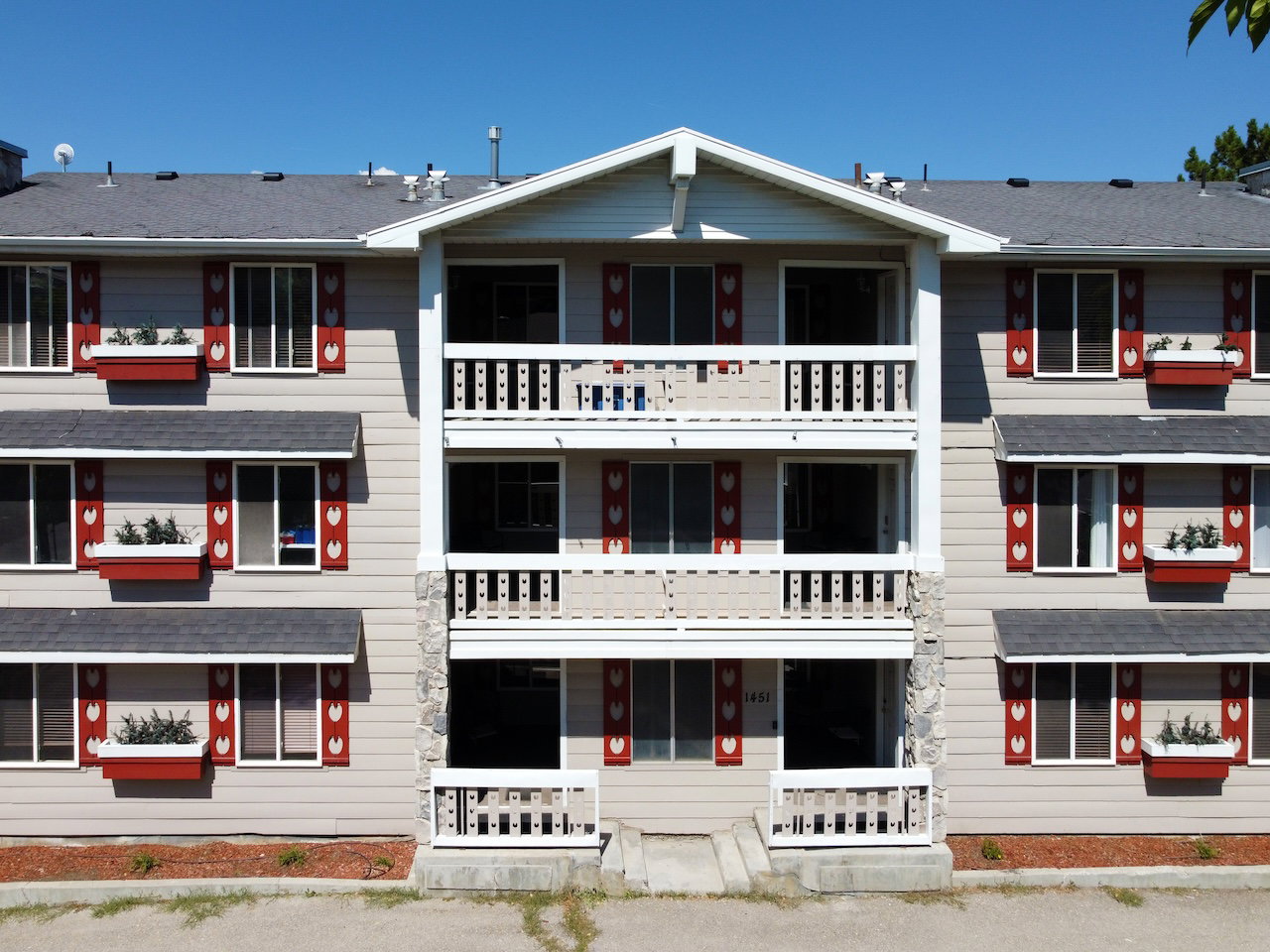 Multi-story exterior featuring neutral siding, red decorative shutters, and white window boxes