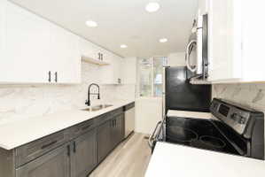 Contemporary kitchen featuring two-tone cabinetry, a dual-basin stainless steel sink with a matte black high-arch faucet, sleek white countertops, and a full tile backsplash