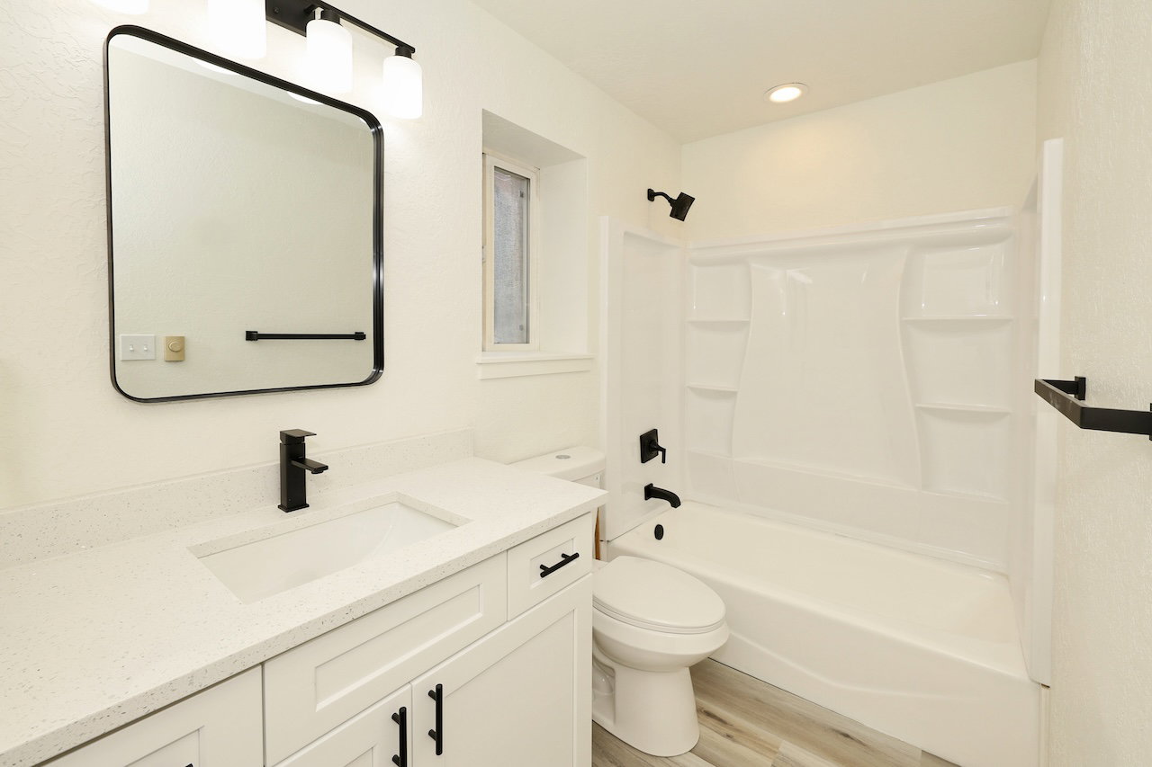 Bathroom featuring a white vanity with integrated sink, quartz-finish countertop, and matte black hardware