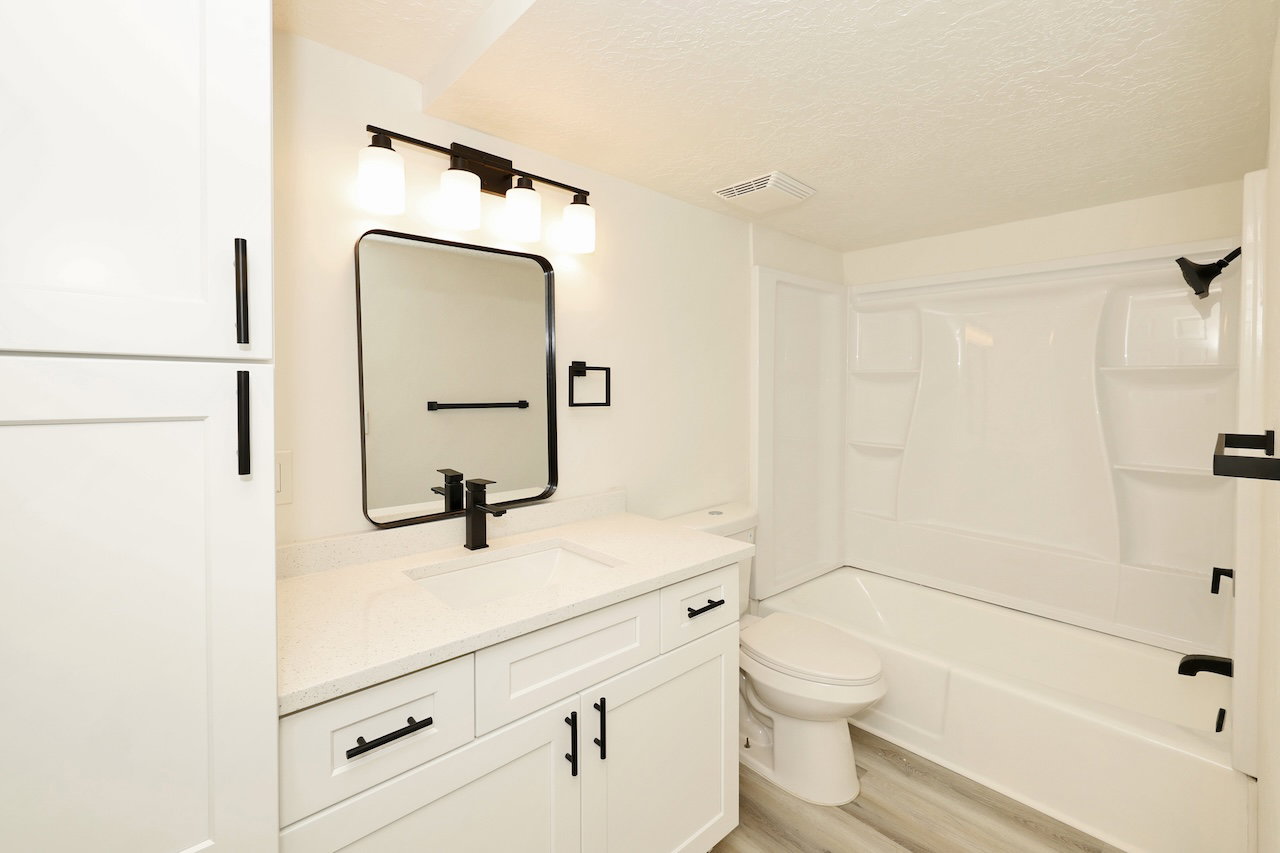 Contemporary bathroom featuring a white vanity with a light-colored countertop, a rectangular black-framed mirror, and a modern black faucet