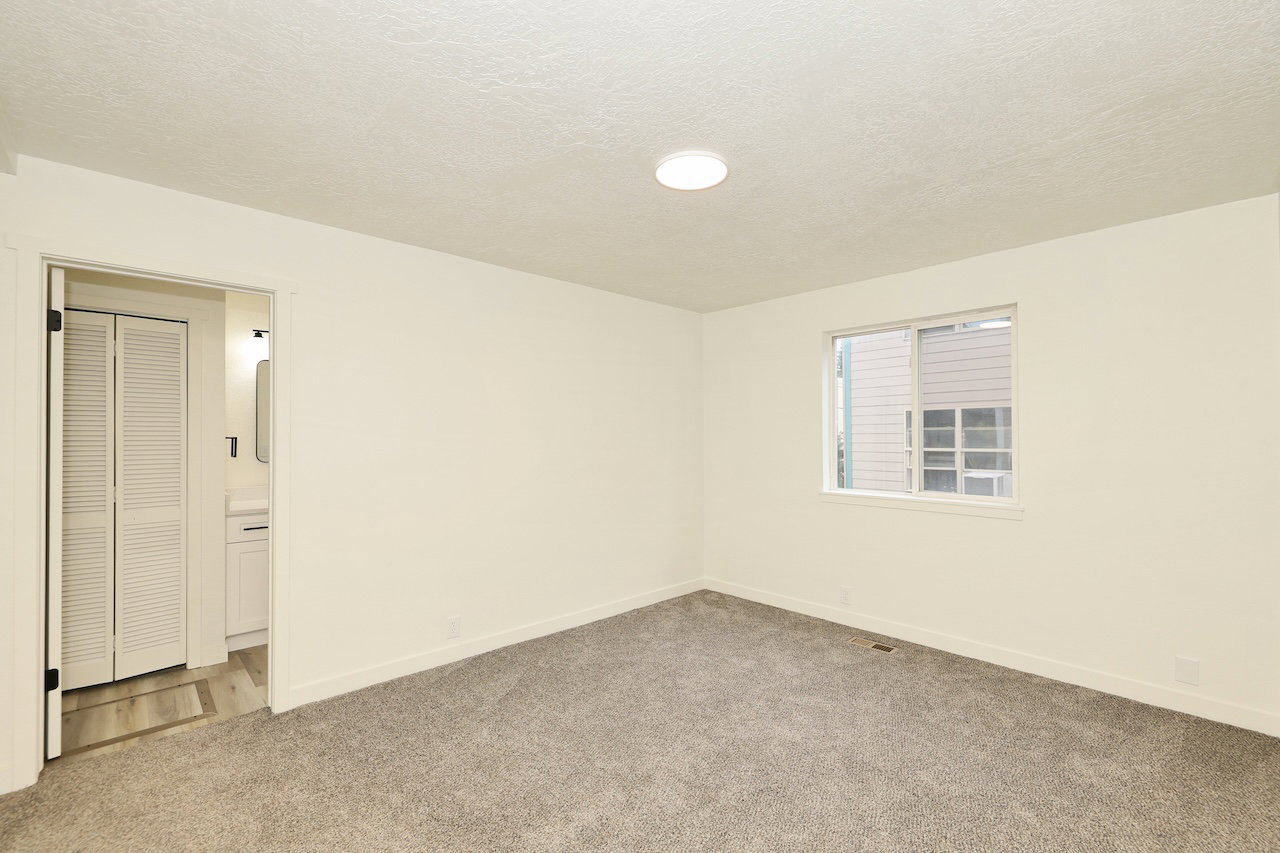 Neutral wall paint, gray carpet flooring, and a single window with white trim