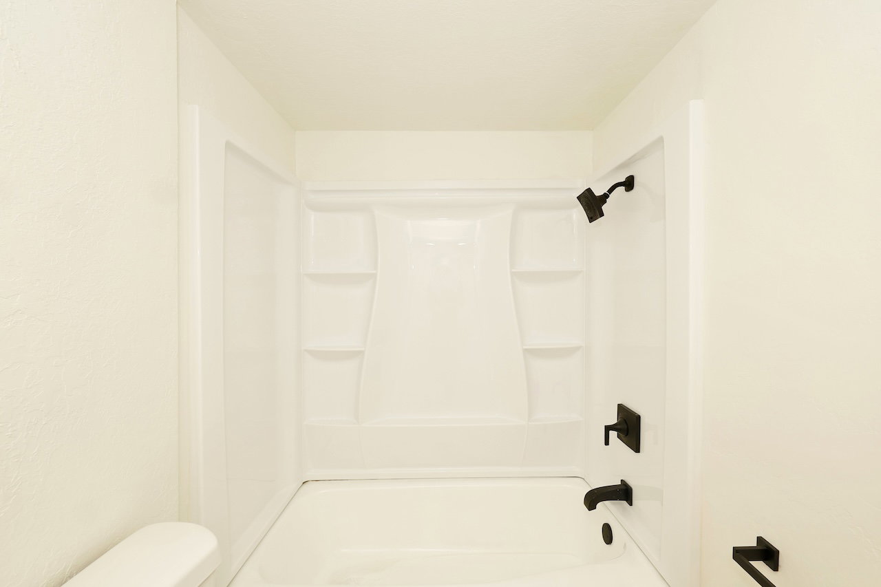 Bright white tub and shower combination featuring black fixtures, built-in shelving, and a modern aesthetic