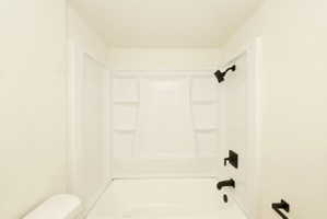 Bright white tub and shower combination featuring black fixtures, built-in shelving, and a modern aesthetic