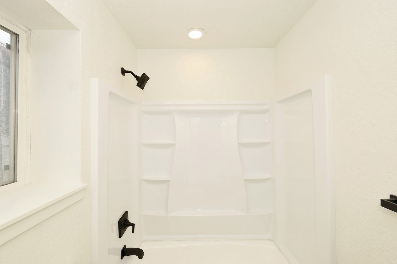 Bathtub and shower combination featuring a white surround, matte black fixtures, recessed lighting, and a window with white trim