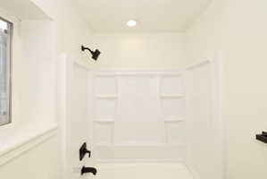 Bathtub and shower combination featuring a white surround, matte black fixtures, recessed lighting, and a window with white trim